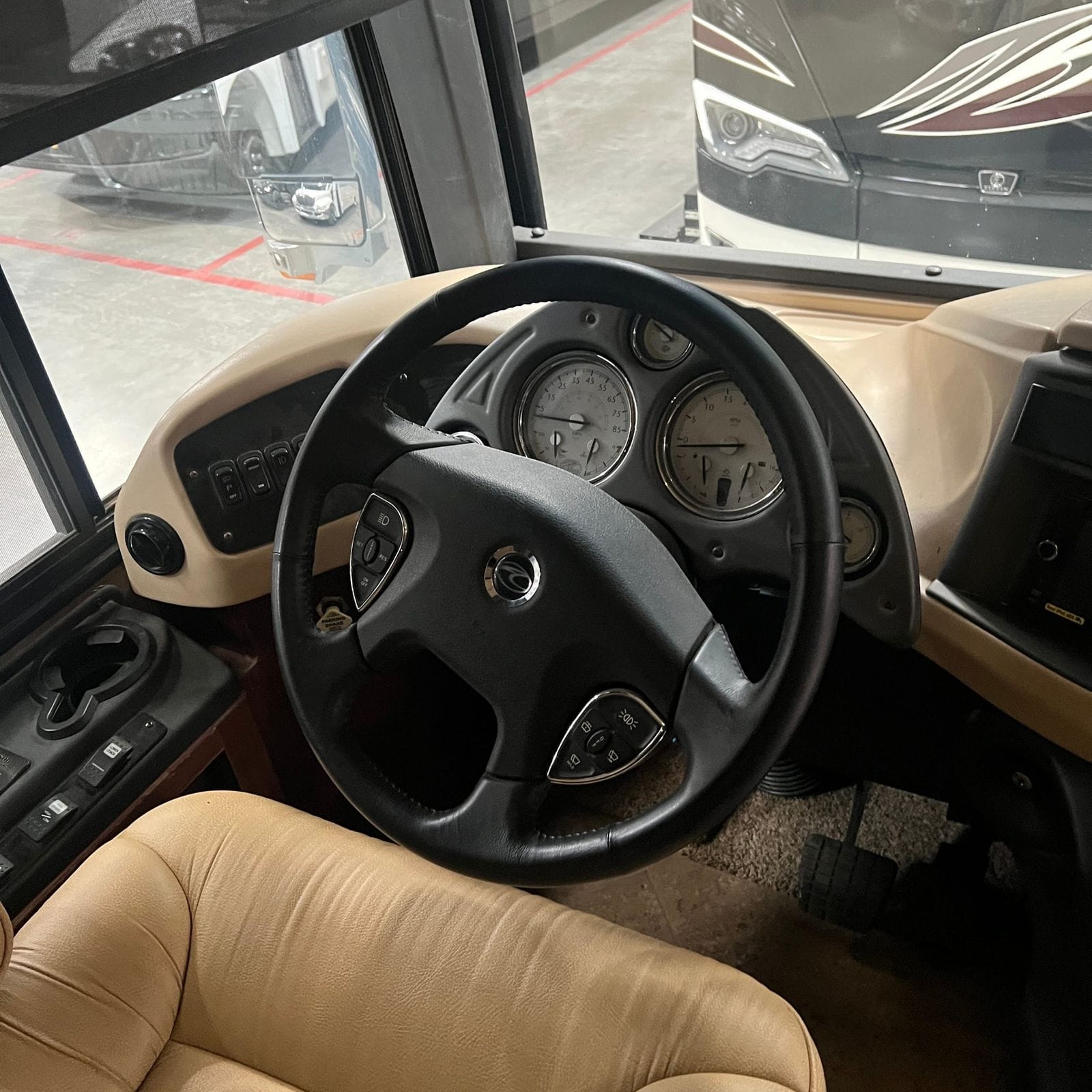 2013 American Coach American Revolution 42T driver's station showing steering wheel, gauge cluster, tan leather driver seat, driver window and side mirror