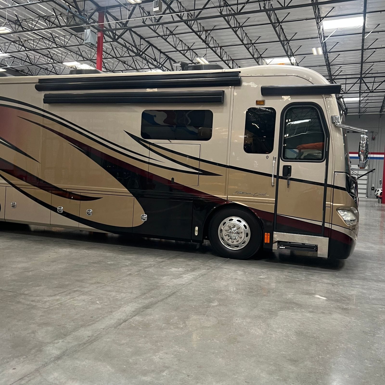 2013 American Coach American Revolution 42T passenger-side full profile of the tan and burgundy Class A diesel pusher, front cap and headlight in frame, awnings retracted and slides in