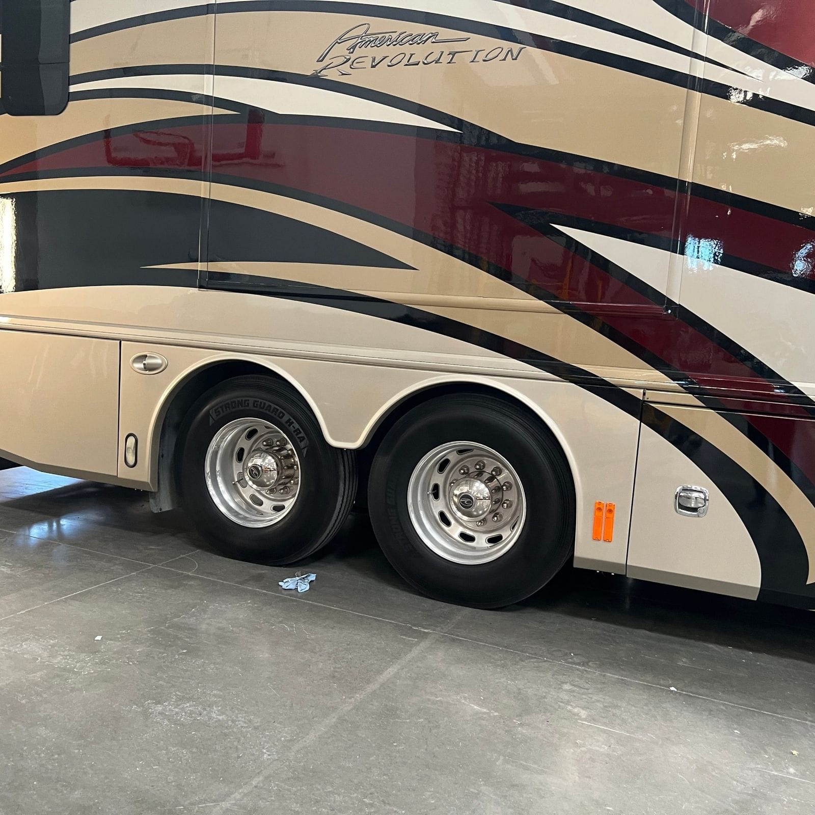 2013 American Coach American Revolution 42T close view of the tandem drive and tag axle polished aluminum wheels and tires below a baggage door