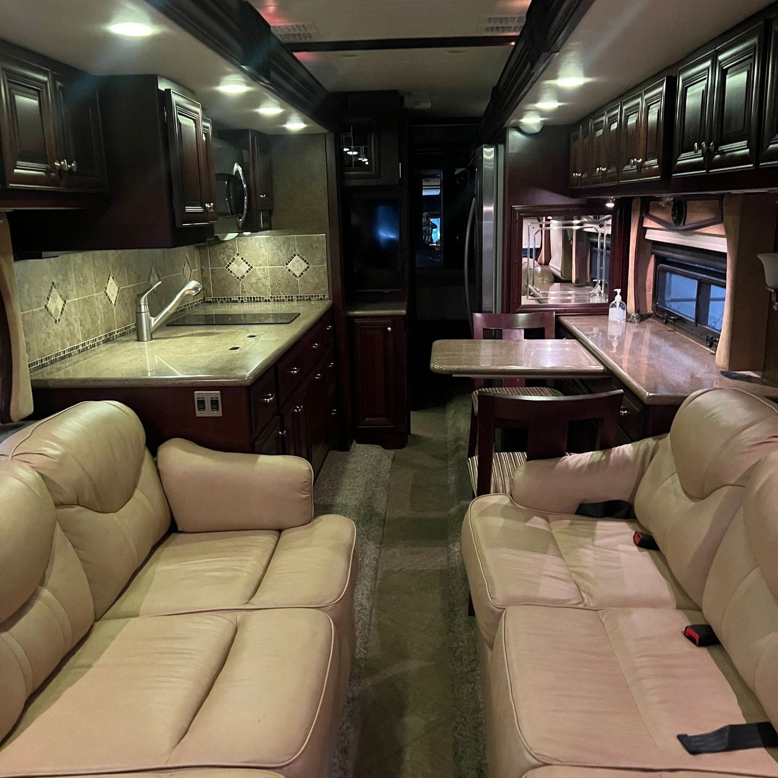 2013 American Coach American Revolution 42T living area looking aft from the cockpit over two facing leather sofas toward the galley, dinette and polished tile aisle