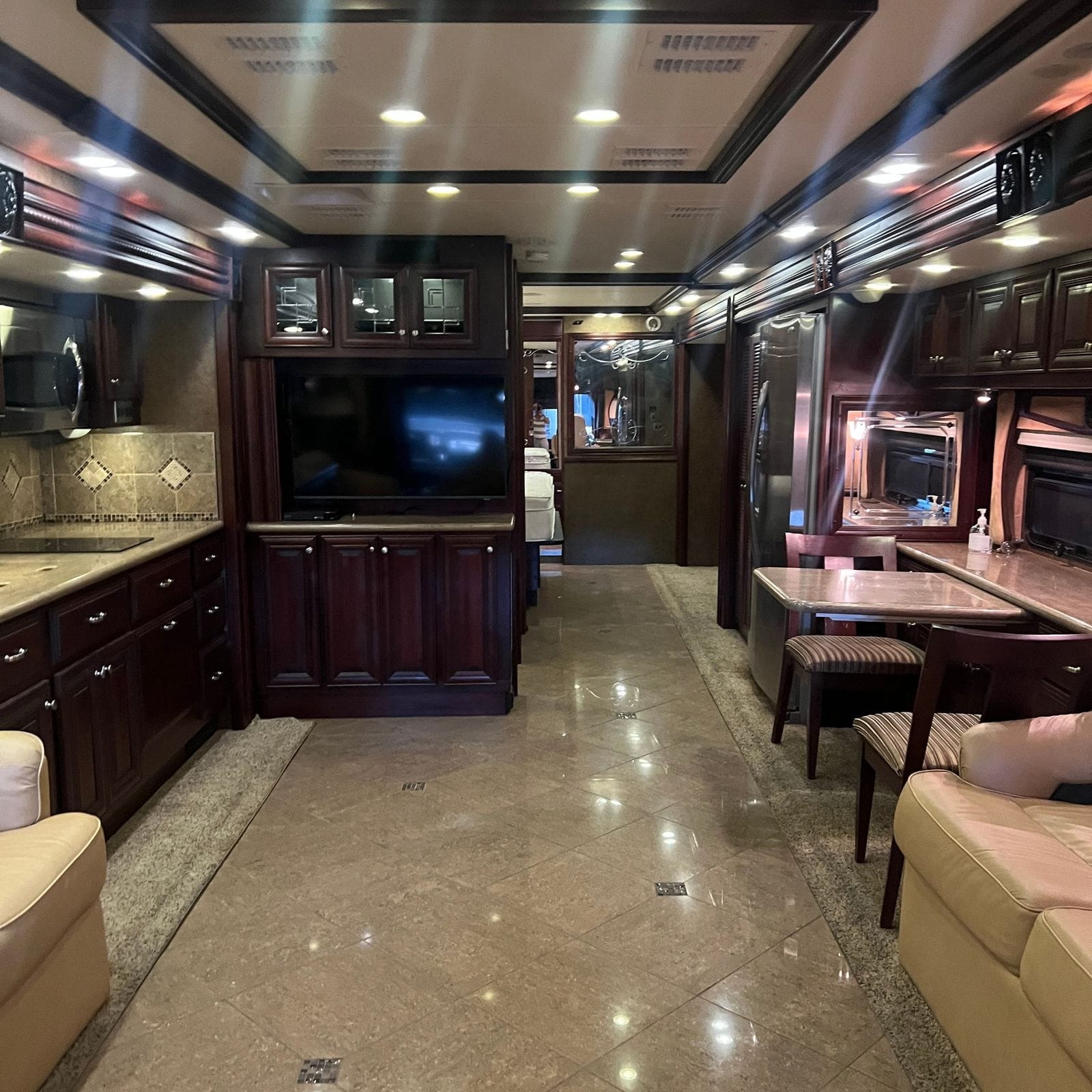 2013 American Coach American Revolution 42T full-length view aft with galley and cooktop at left, cherry entertainment cabinet, stainless refrigerator and L-shaped dinette at right
