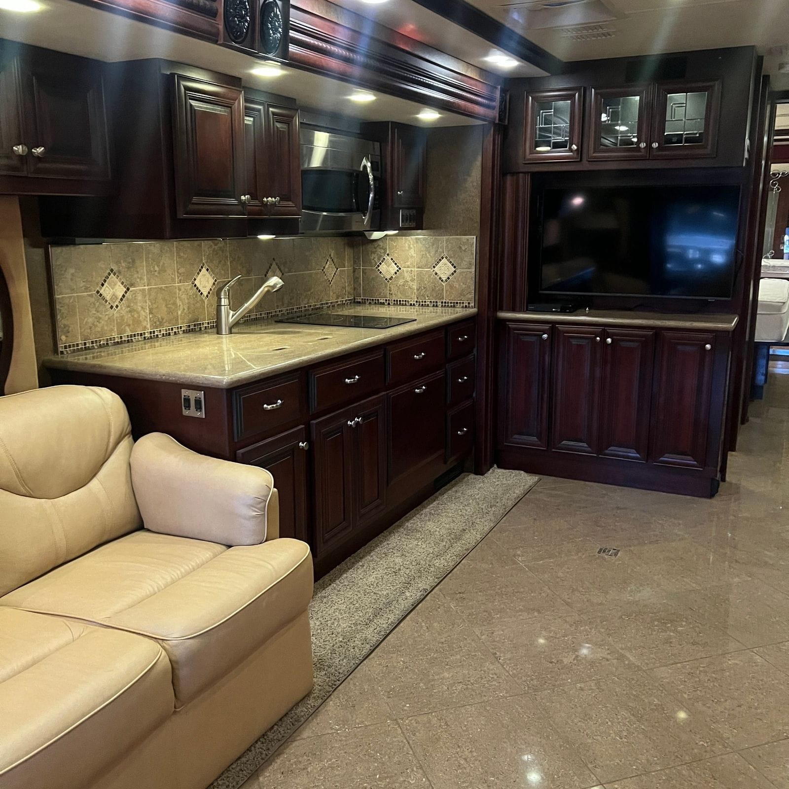2013 American Coach American Revolution 42T galley overview with solid-surface counter, two-burner cooktop, stainless microwave and cherry cabinetry