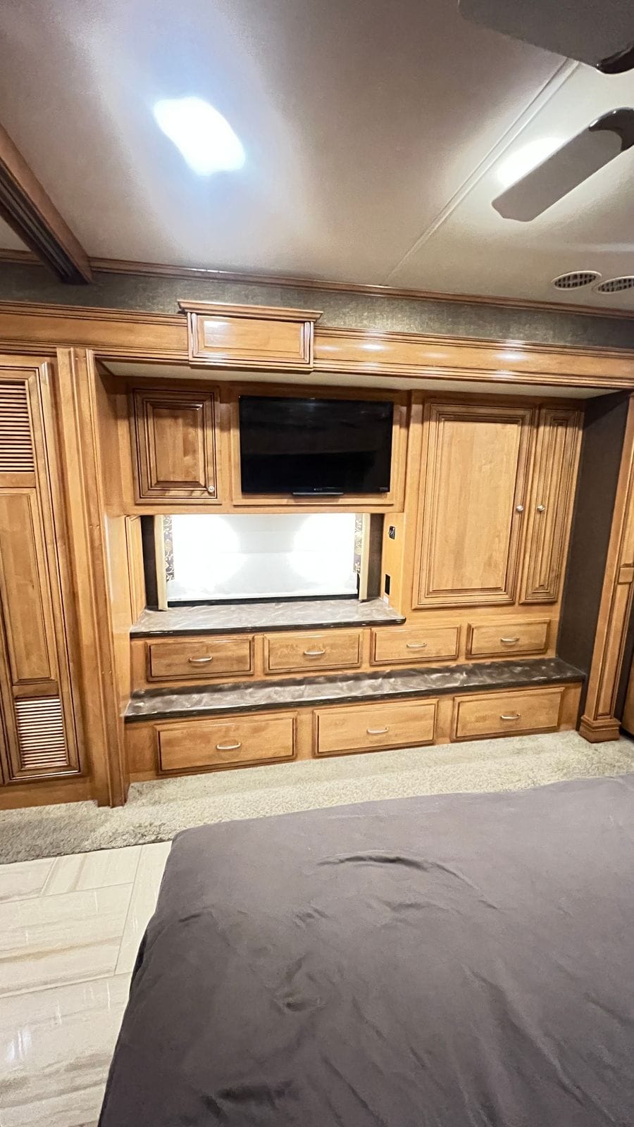 2016 Thor Tuscany 45AT bedroom wall opposite the bed with a flat-screen television, shaded window, dresser drawers under stone-look tops and wardrobe doors