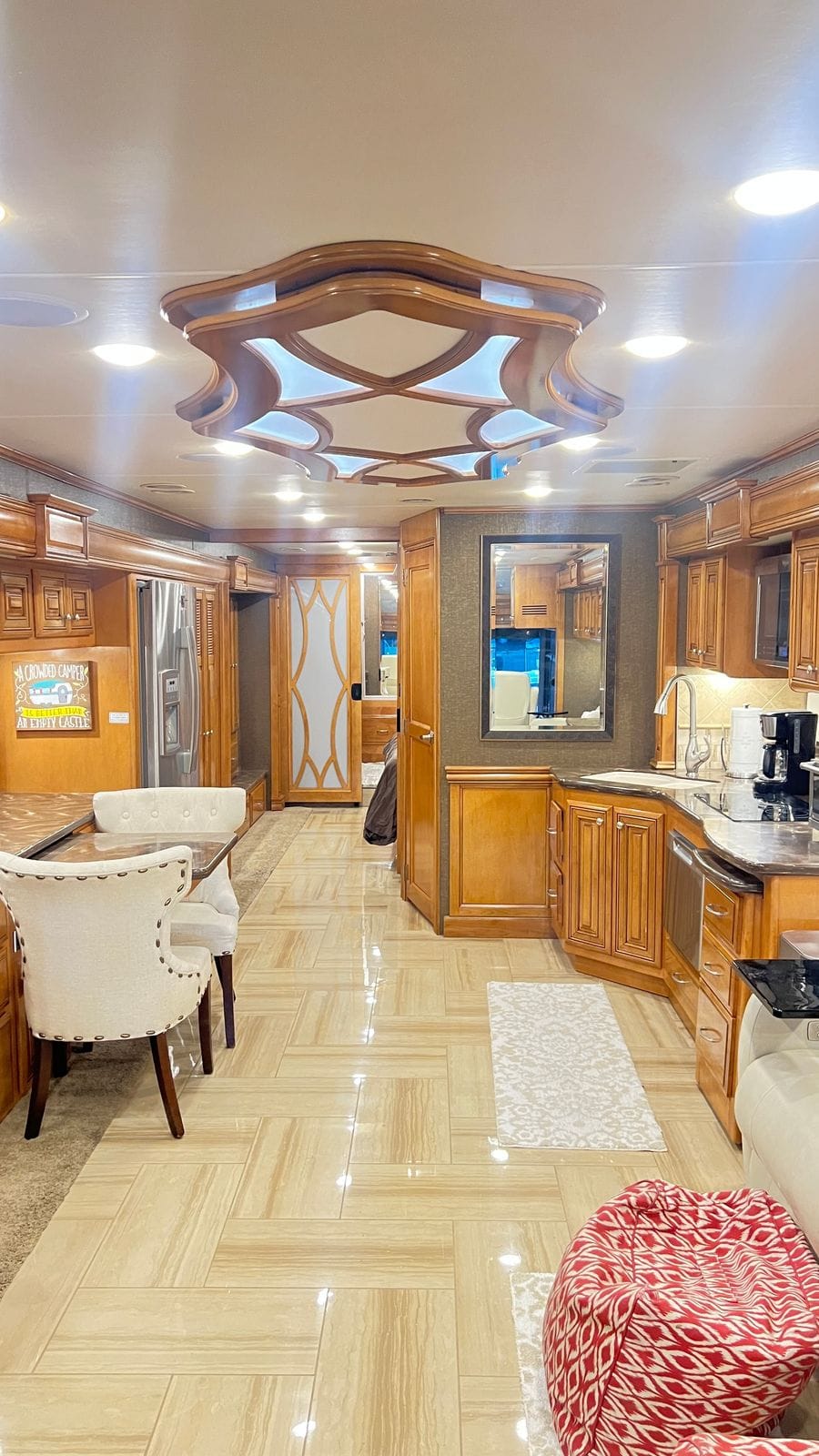 2016 Thor Tuscany 45AT interior looking aft down the aisle with a carved wood ceiling medallion, glazed maple cabinetry, stainless french-door refrigerator, L-shaped galley and porcelain tile floor