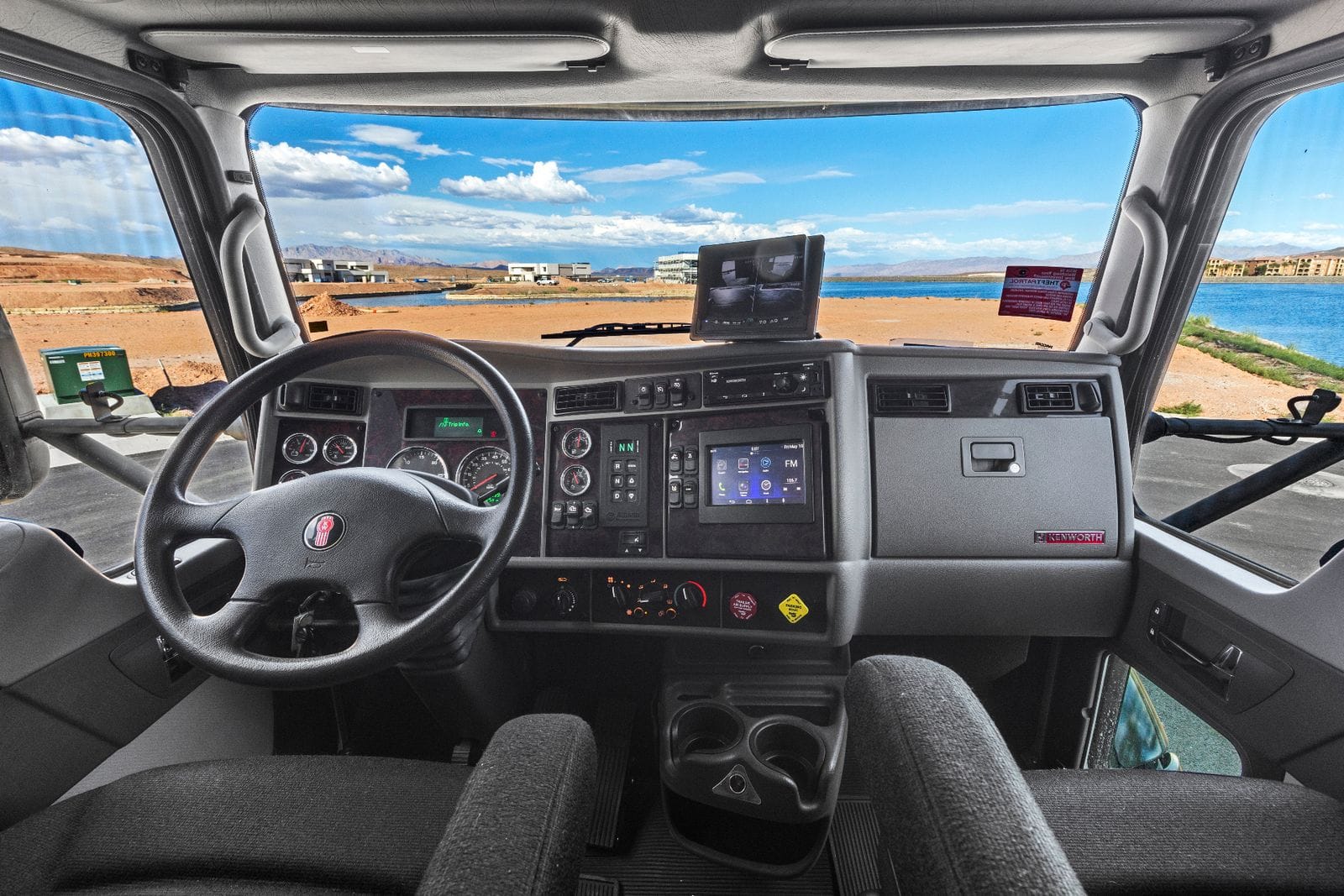2017 Global Expedition Vehicles The Beast cockpit view from inside the cab showing the steering wheel, analog gauge cluster, touchscreen radio, backup-camera monitor on the dash and cloth bucket seats