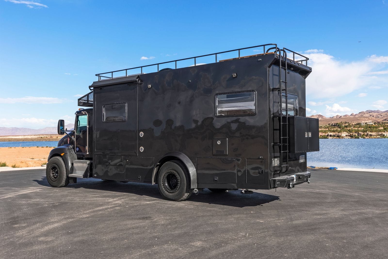 2017 Global Expedition Vehicles The Beast daylight rear driver's-side three-quarter view showing the rear-mounted exterior storage cabinets, full-height rear ladder, roof railing and heavy-duty rear step bumper