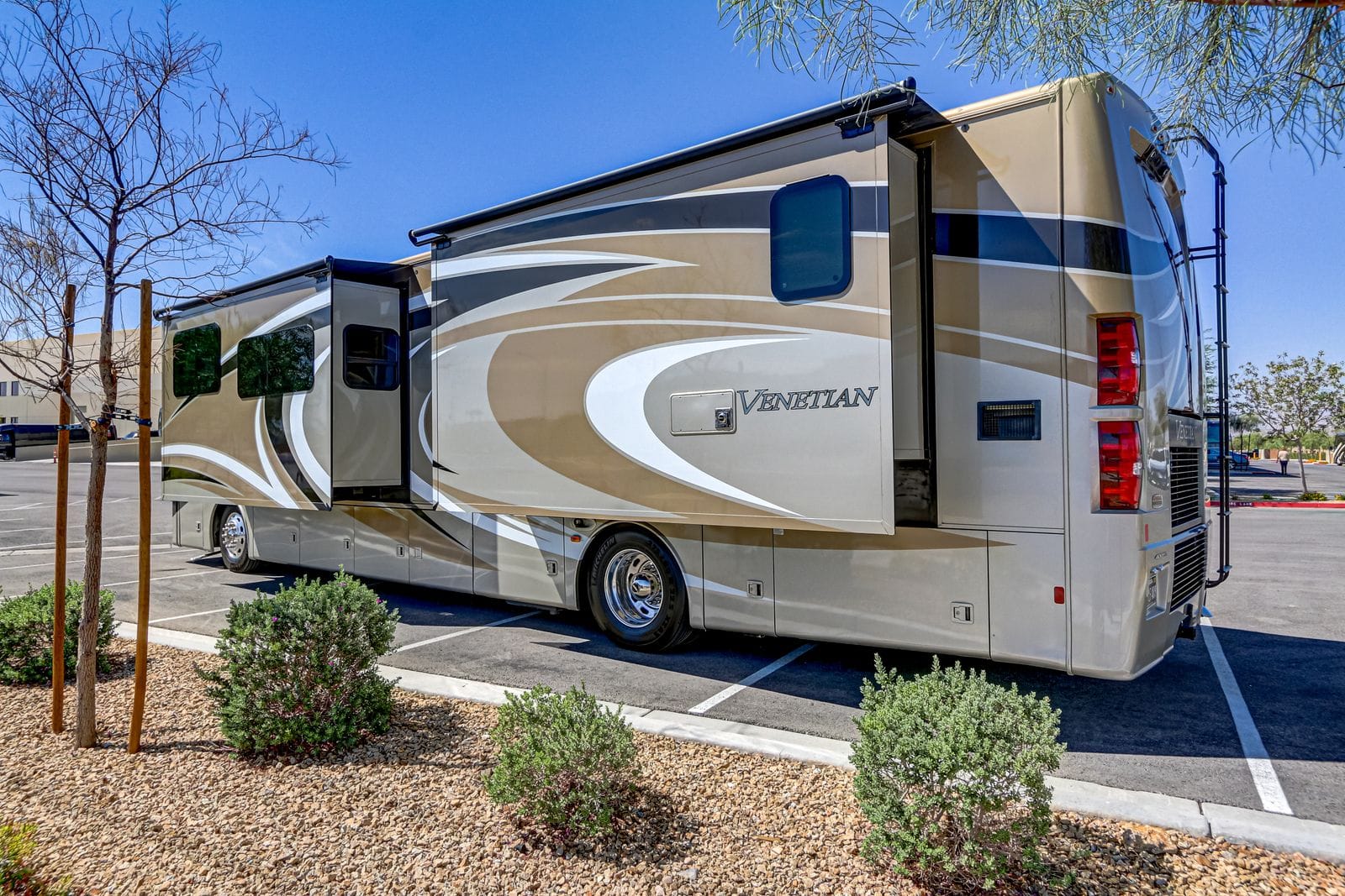 2017 Thor Venetian 40A driver-side rear three-quarter view with both slide-outs extended and the awning rolled out, Venetian script and a flush utility hatch on the side wall, desert landscaping in the foreground