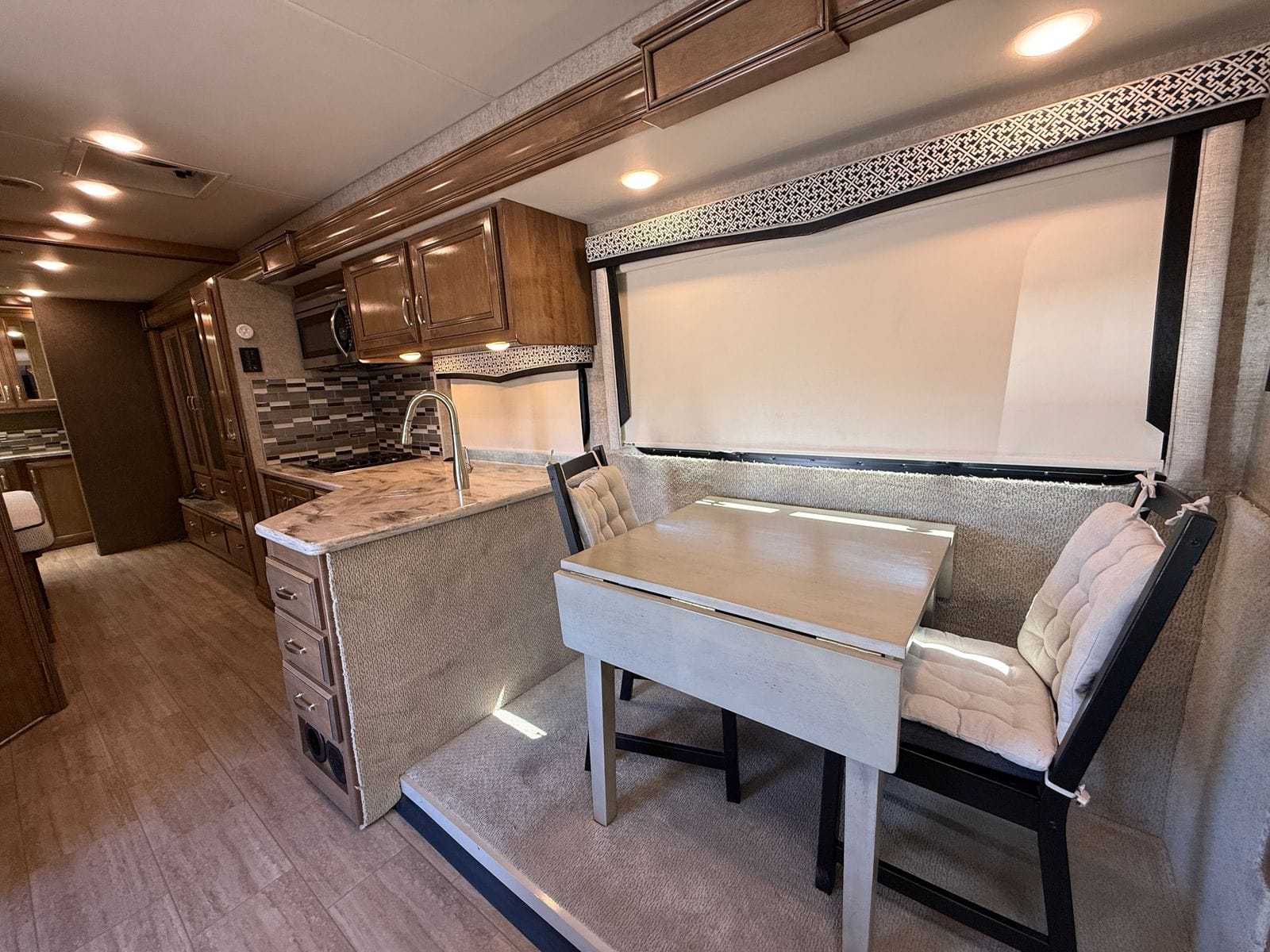 2020 Thor Magnitude BH35 dinette on the slide-out, a freestanding drop-leaf table with two cushioned chairs beneath the window, with the galley beyond