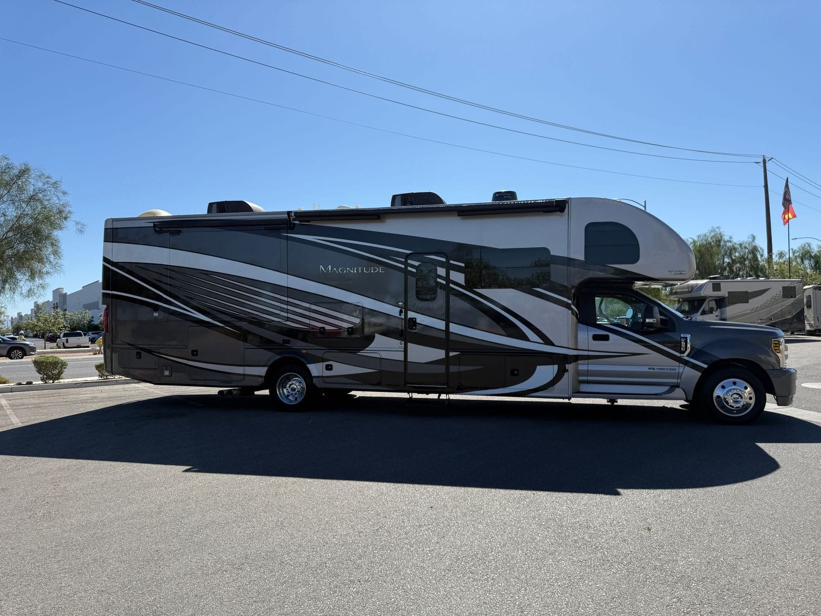 2020 Thor Magnitude BH35 full passenger-side profile, showing the silver and charcoal body graphics, patio awning, entry door and the Ford Super Duty cab