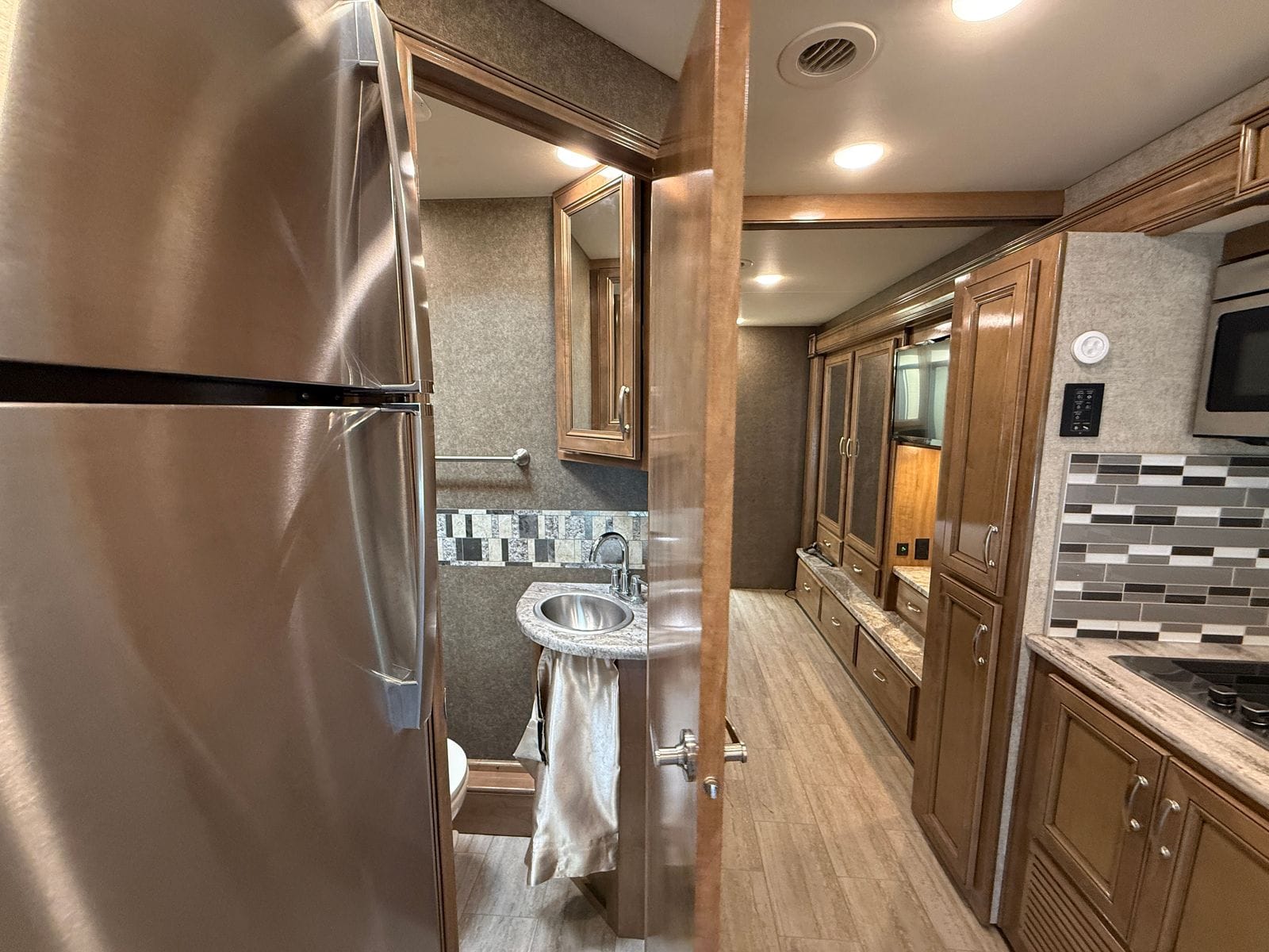 2020 Thor Magnitude BH35 hallway looking aft past the refrigerator and the open half-bath door, toward the bedroom wardrobe wall, with the galley counter at right