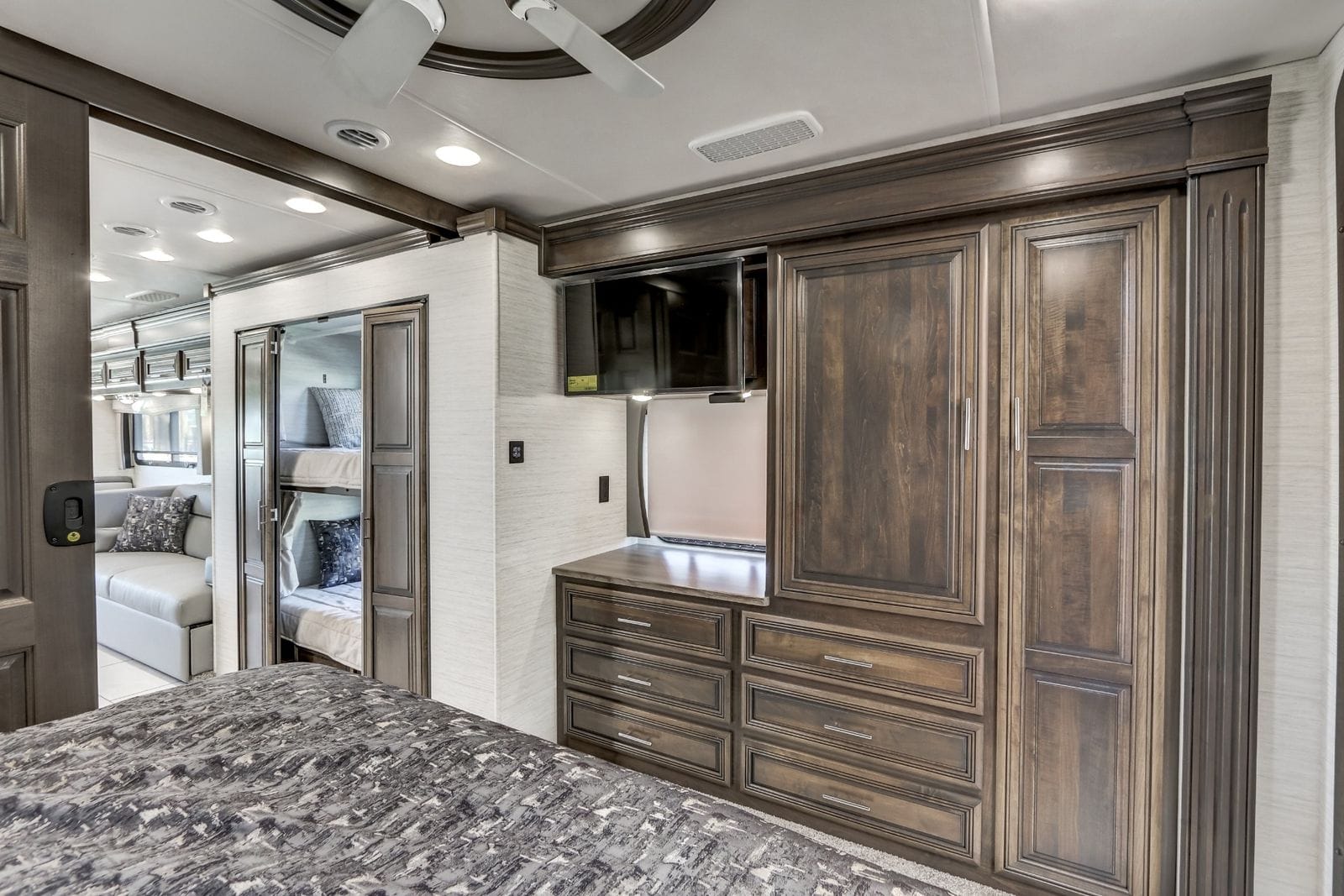 2024 Forest River Berkshire XL 40E bedroom dresser wall with six drawers, wardrobe cabinetry and swing-arm LED TV, with the bunk beds visible through the open bunk-room door