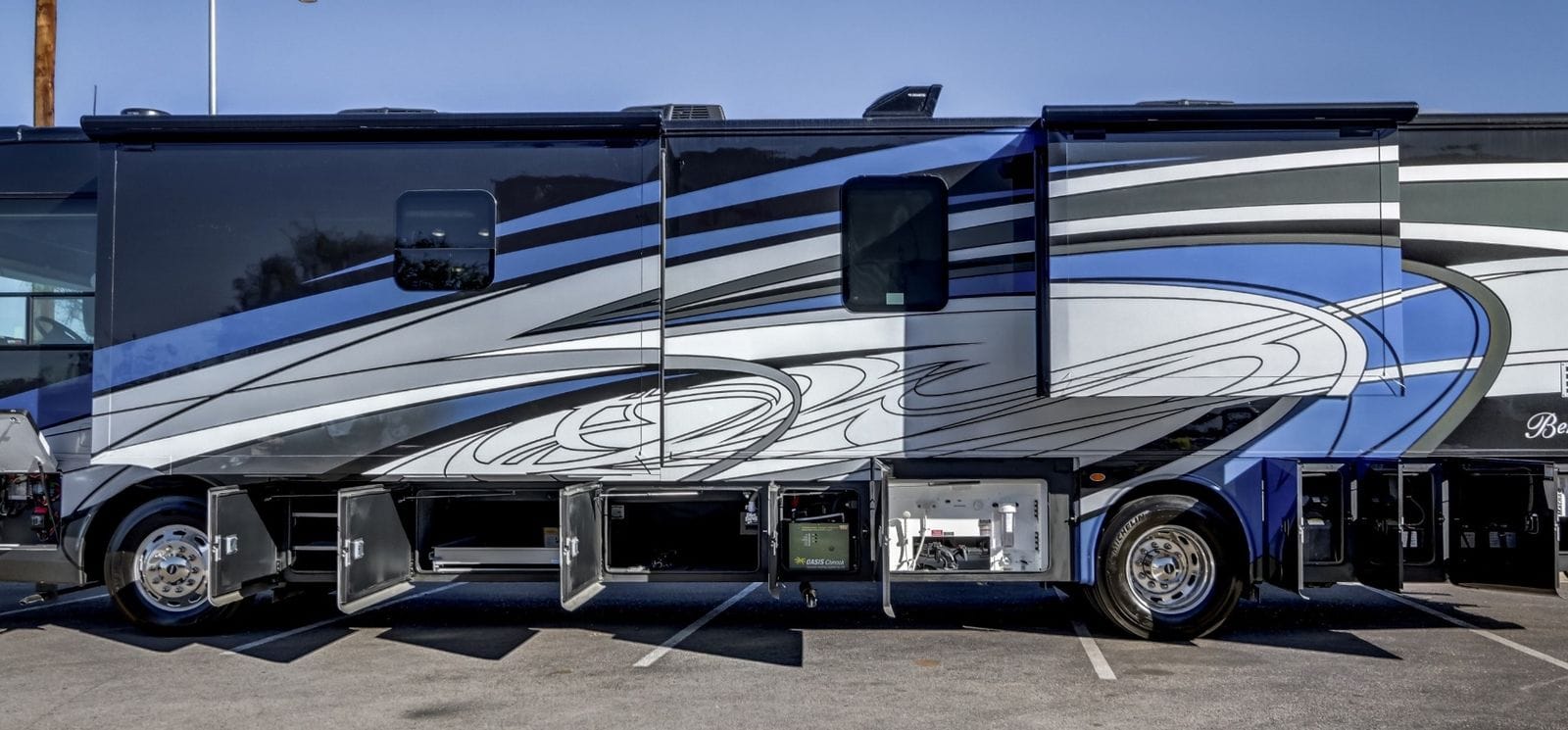 2024 Forest River Berkshire XL 40E driver's-side mid-body view with storage bays open, showing the Oasis hydronic bay and generator compartment below the slide-outs