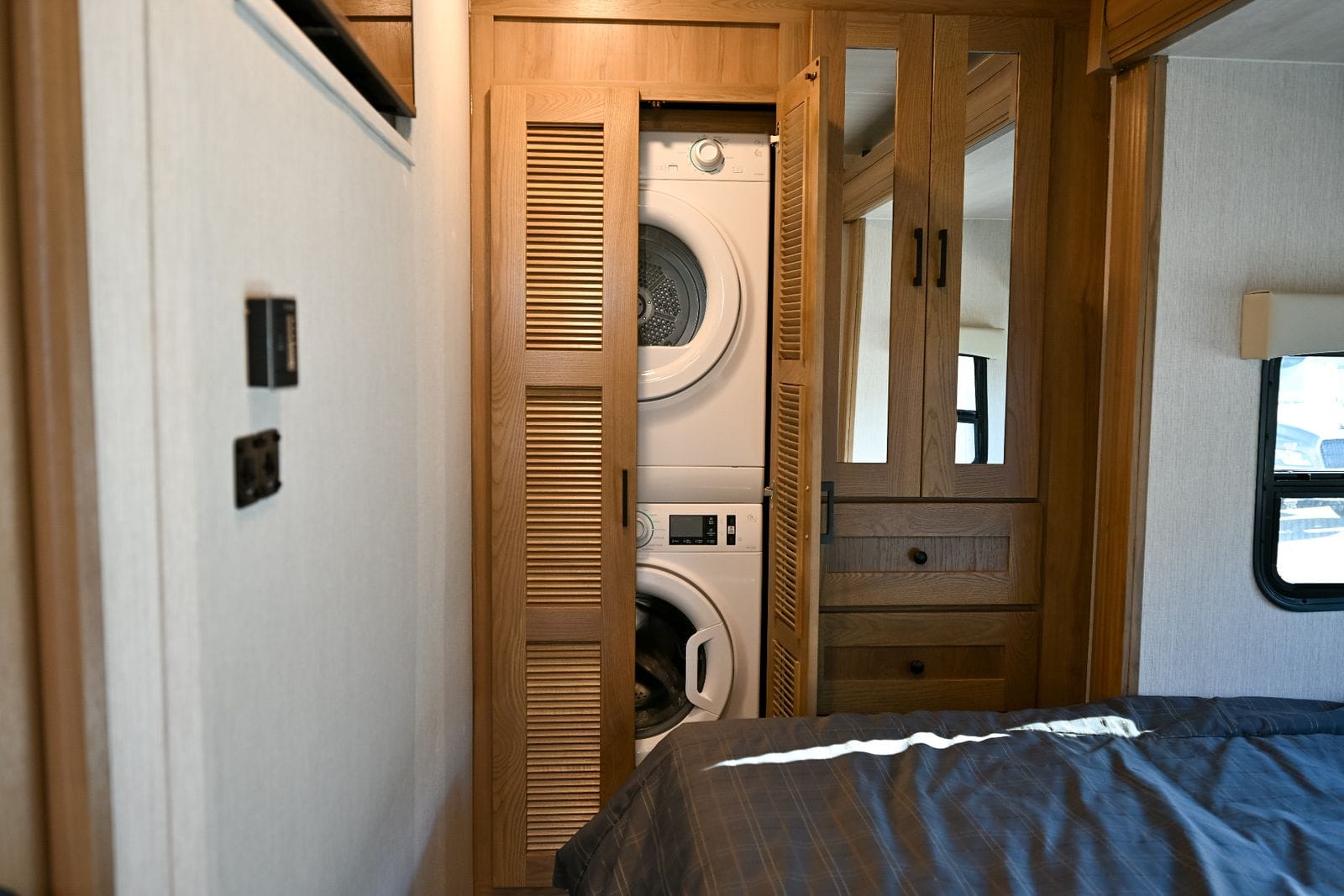 2026 Nexus Maximus 34MX stacked washer and dryer beside the mirrored wardrobe, seen from the foot of the bed