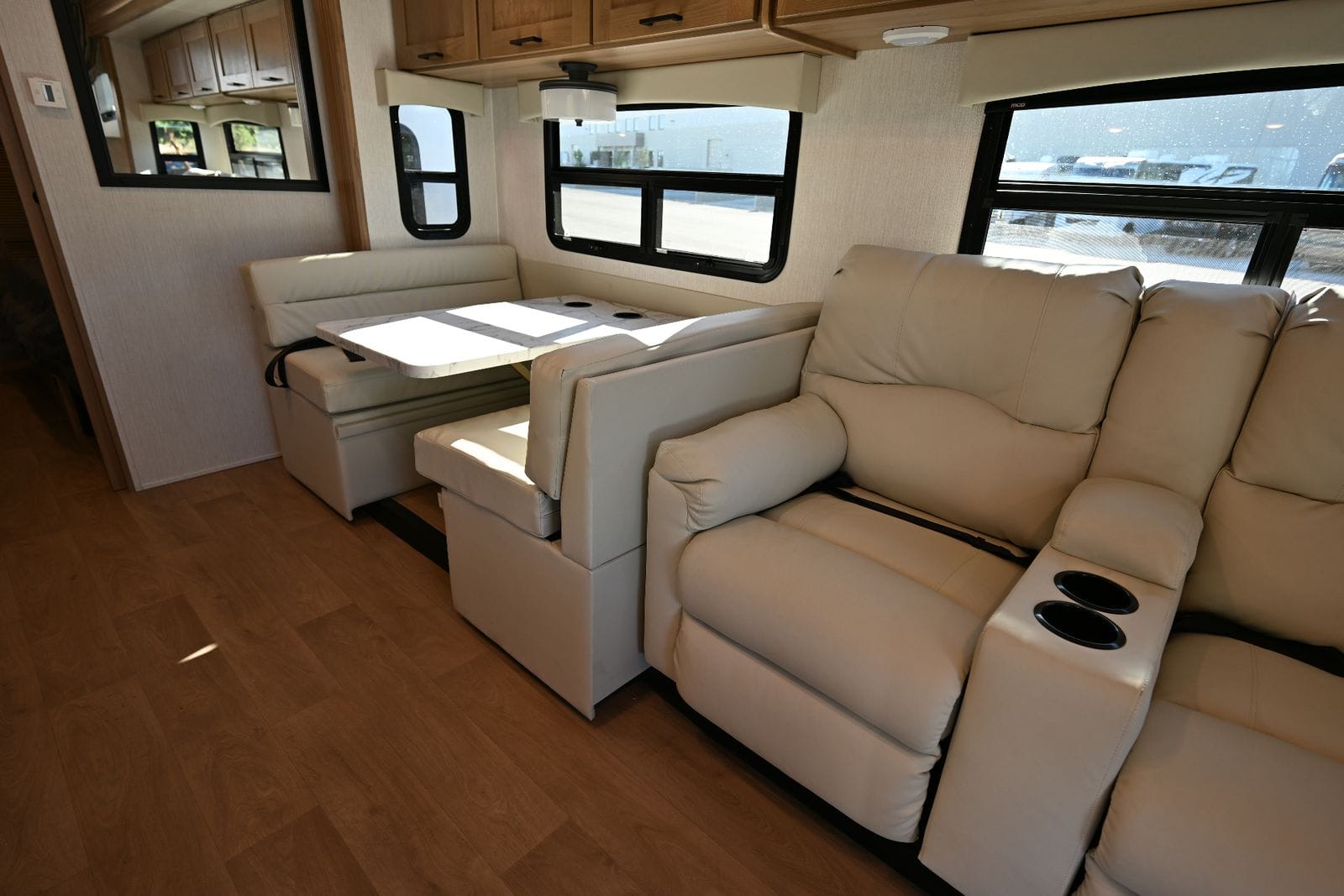 2026 Nexus Maximus 34MX living area looking forward with U-shaped dinette, theater-seat recliners and hardwood-look flooring