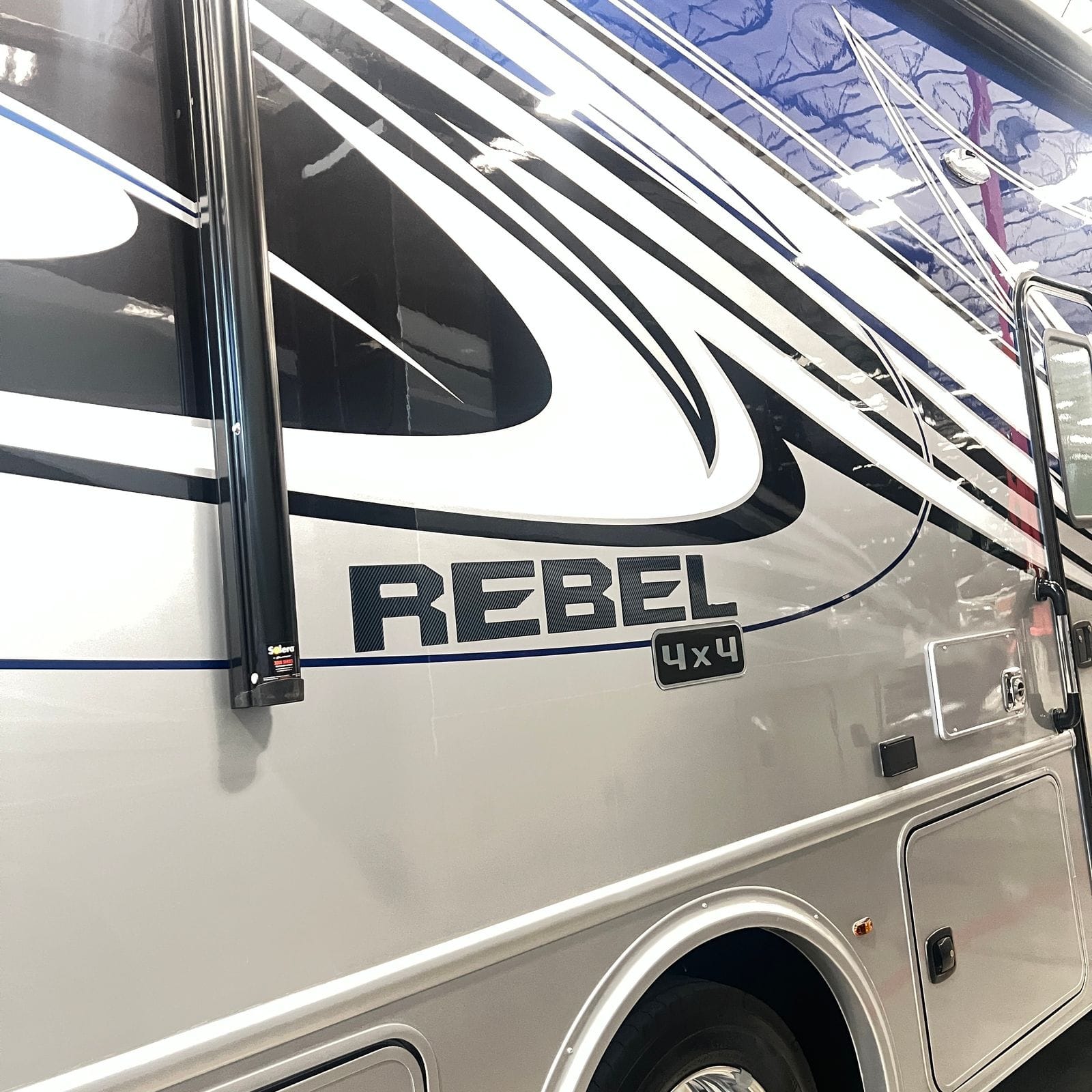 2026 Nexus Rebel 35R close-up of the Rebel badge and 4x4 plaque on the silver sidewall with black and blue swoosh graphics and a Solera awning rail