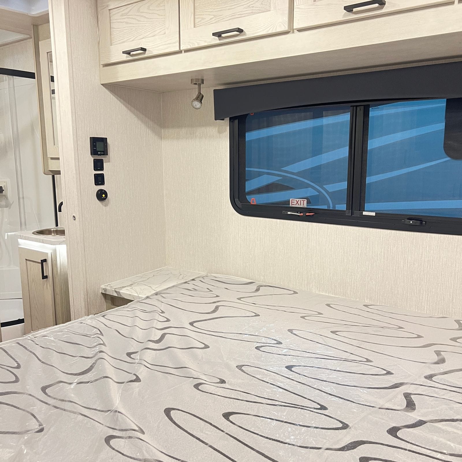 2026 Nexus Rebel 35R rear bed with a marble-look nightstand shelf, control panel, reading light and an emergency-exit slider window
