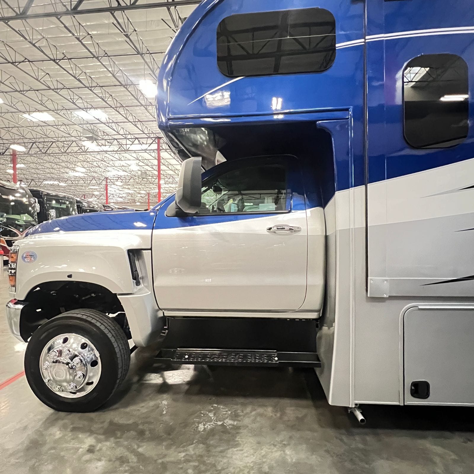2026 Nexus Rebel 35R driver-side profile of the cab and cab-over showing the blue upper body, white cab door, tow mirror and chrome wheel simulator