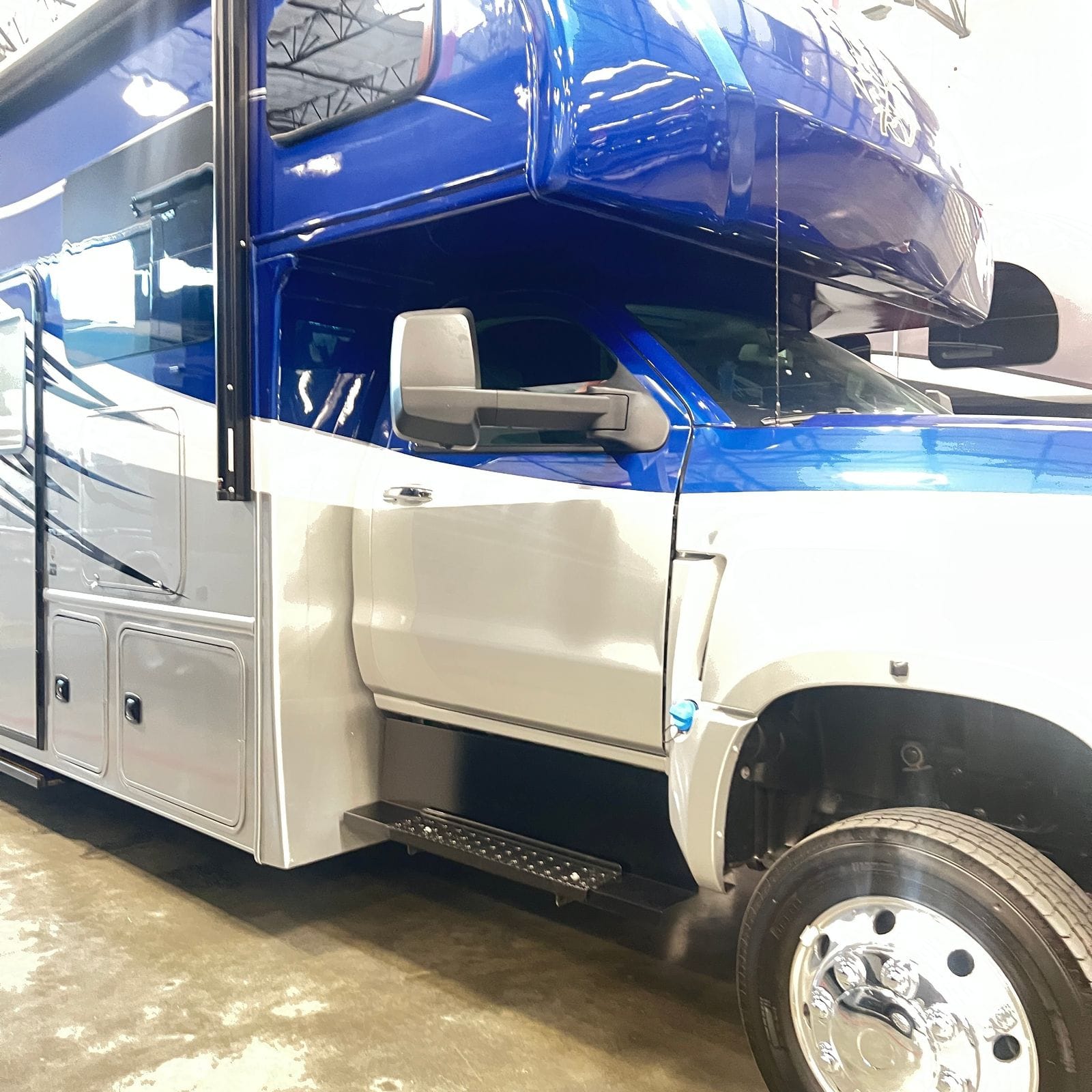 2026 Nexus Rebel 35R passenger-side view of the cab door, tow mirror and forward silver storage compartments beneath the blue cab-over