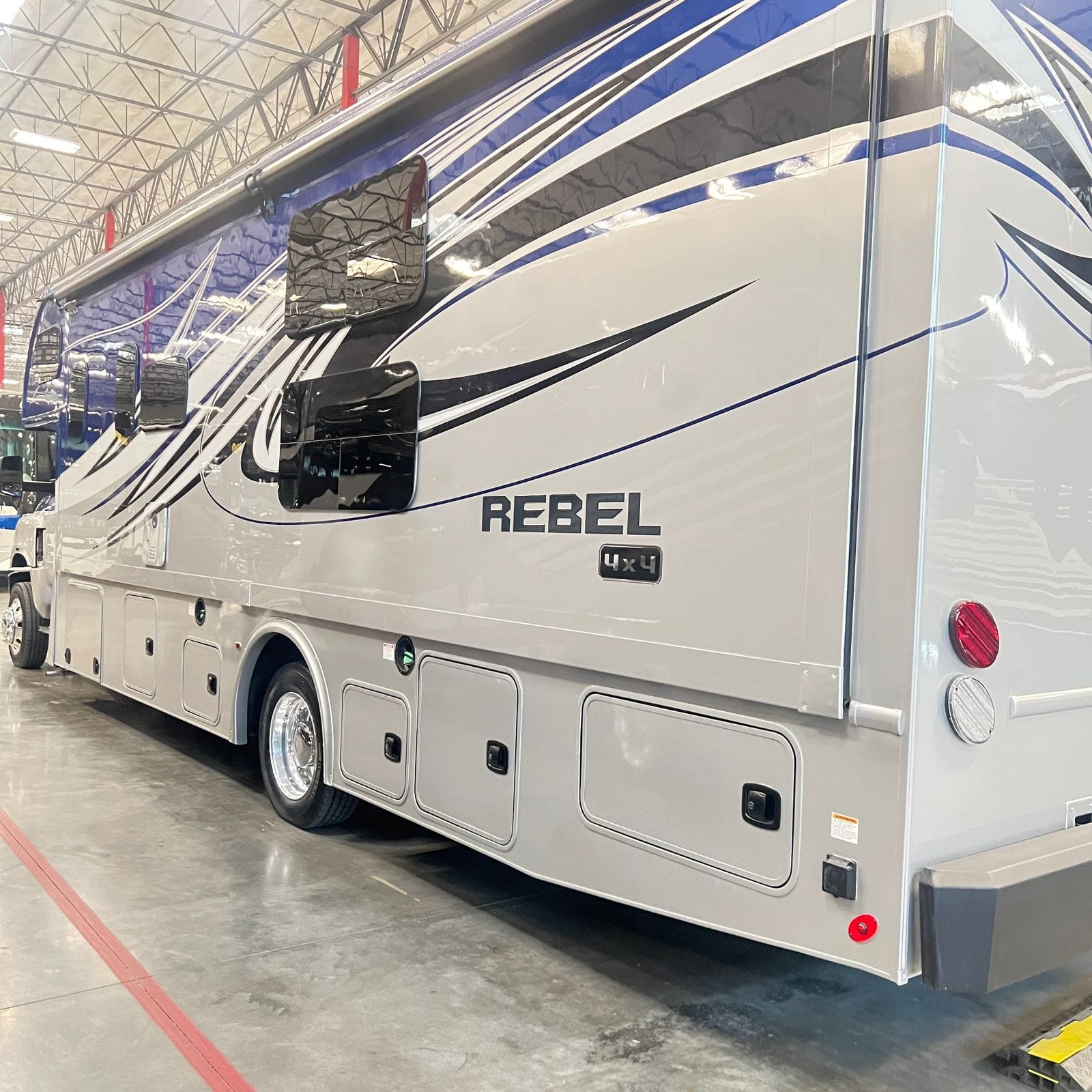 2026 Nexus Rebel 35R rear driver-side three-quarter view showing the full silver body length, Rebel 4x4 badge, three storage bay doors, awning and round tail lamps