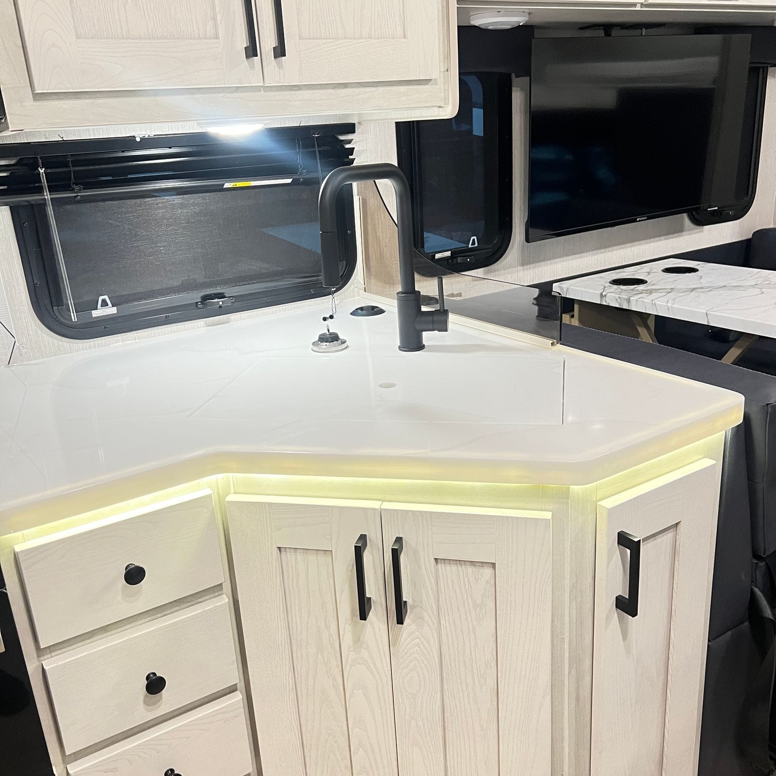 2026 Nexus Rebel 35R galley showing the sink, black faucet, lighted countertop edge and lower cabinets, with the television and dinette beyond