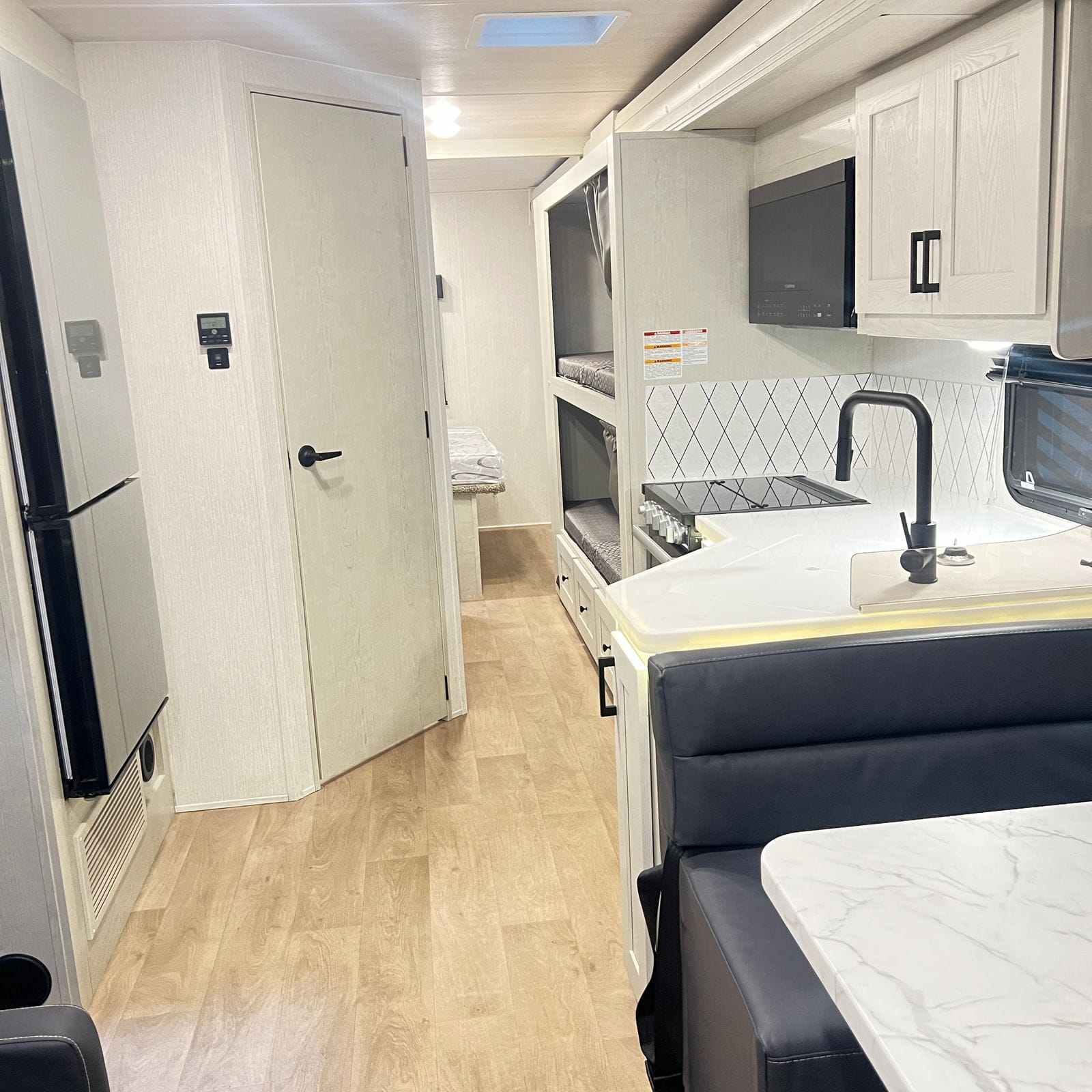 2026 Nexus Rebel 35R interior looking aft down the aisle with wood-look flooring, stainless refrigerator, galley, bunk beds and the rear bed beyond