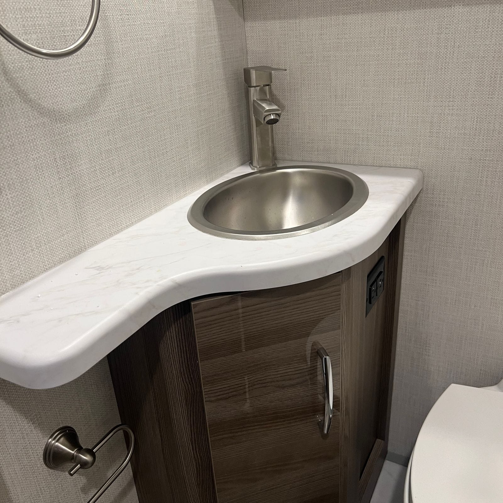 2026 Thor Delano 24XL bathroom vanity close-up with marble-look countertop, round stainless sink, brushed-nickel faucet, towel ring and wood-grain cabinet door beside the toilet