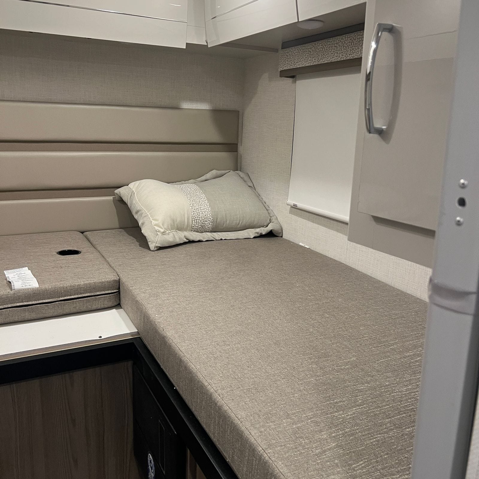 2026 Thor Delano 24XL opposite rear twin bed with beige mattress and pillow, padded wall panels, window with roller shade and gloss white overhead cabinets