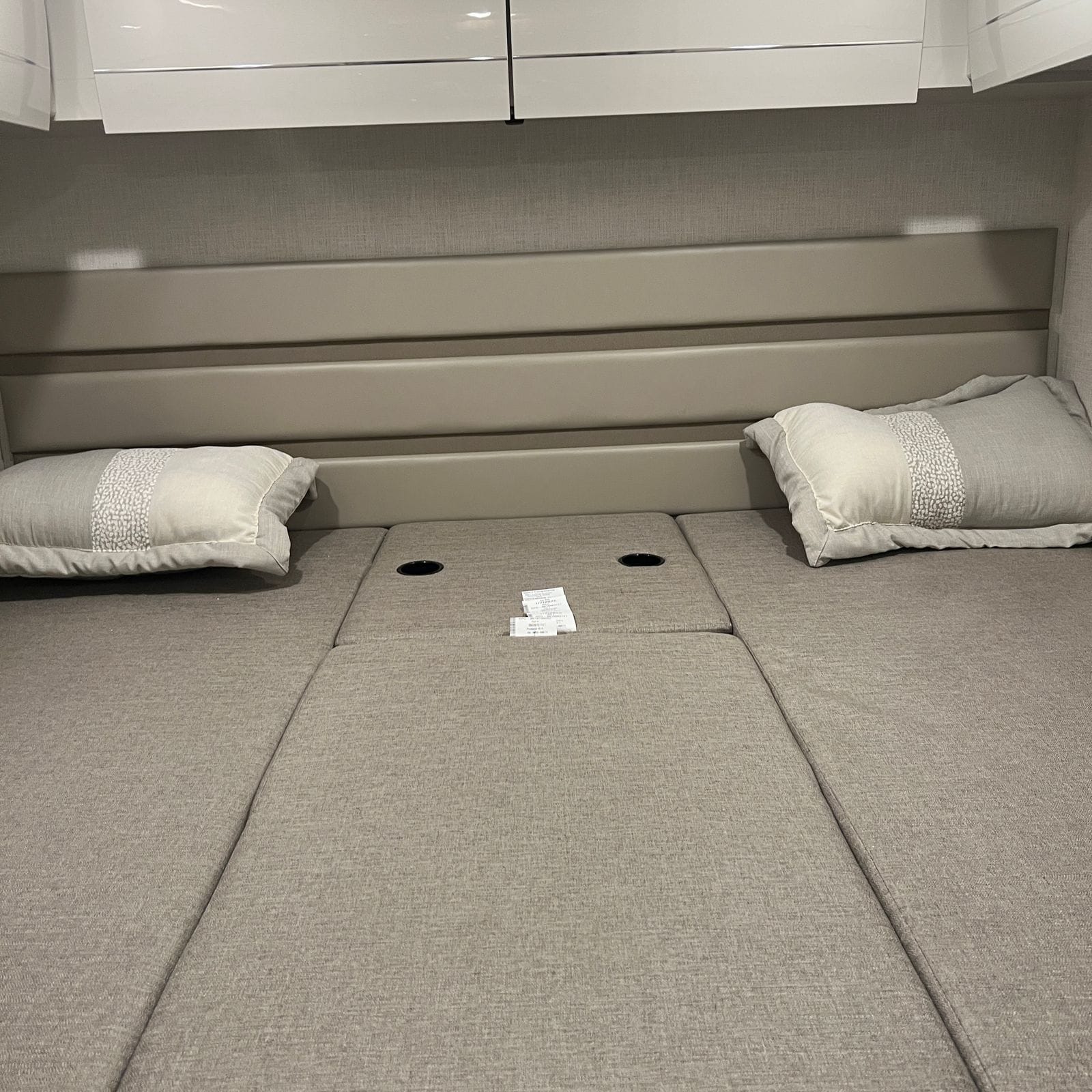2026 Thor Delano 24XL twin beds converted to a king with the infill cushion in place, two pillows against the padded headboard and gloss white overhead cabinets