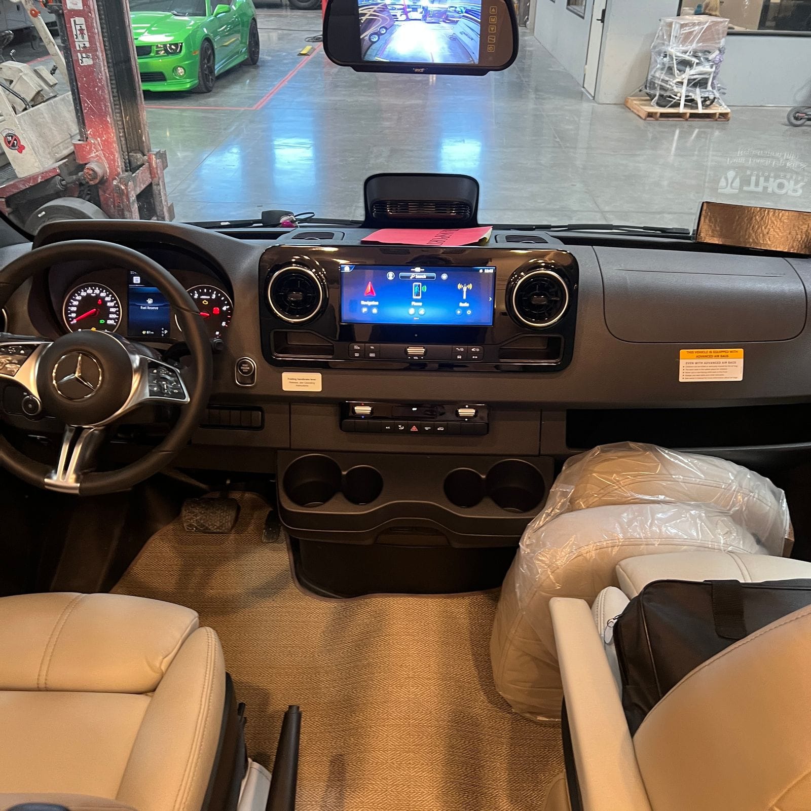 2026 Thor Delano 24XL dashboard seen from between the seats with Mercedes-Benz steering wheel, digital gauge cluster, touchscreen infotainment, rearview monitor and tan leatherette captain's chairs