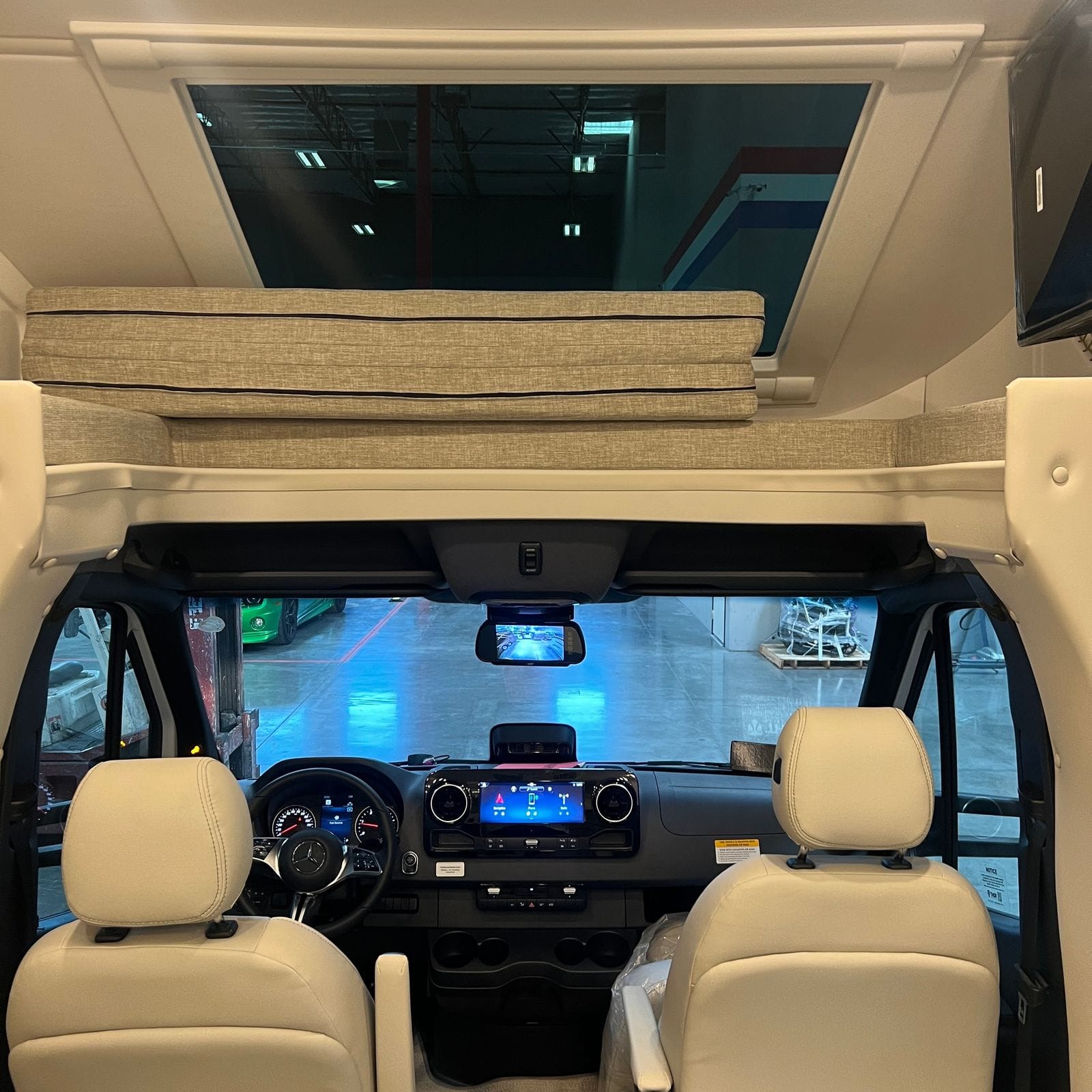2026 Thor Delano 24XL view forward from the living area over the cab-over bunk with folded mattress cushions, an overhead skylight and the two tan captain's chairs beyond