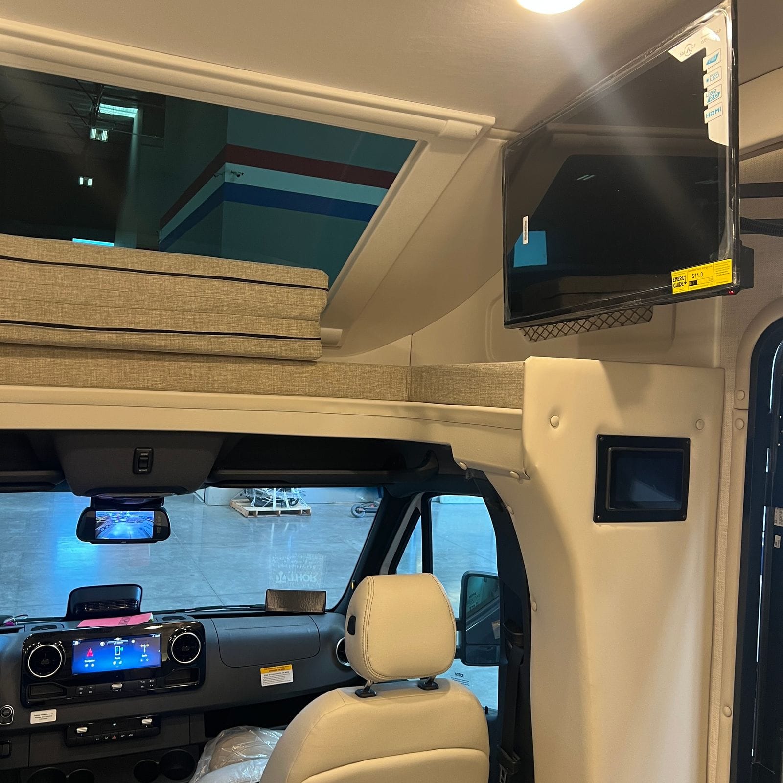 2026 Thor Delano 24XL swing-out flat-screen television mounted beside the cab-over bunk with folded cushions and skylight, above the cockpit
