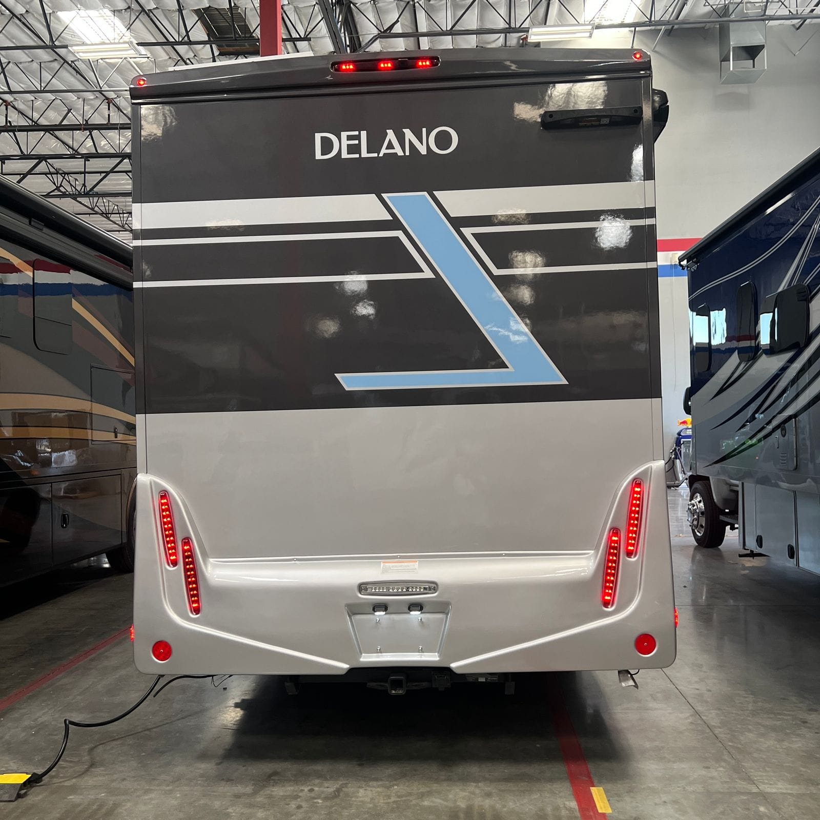 2026 Thor Delano 24XL rear view with Delano lettering, grey, white and light-blue angled graphics, vertical LED tail lights and a hitch receiver