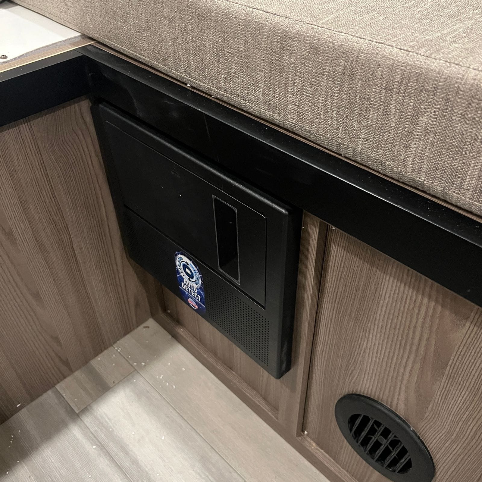 2026 Thor Delano 24XL appliance unit with recessed handle and perforated vent built into wood-grain cabinetry beneath the bed platform, beside a floor register