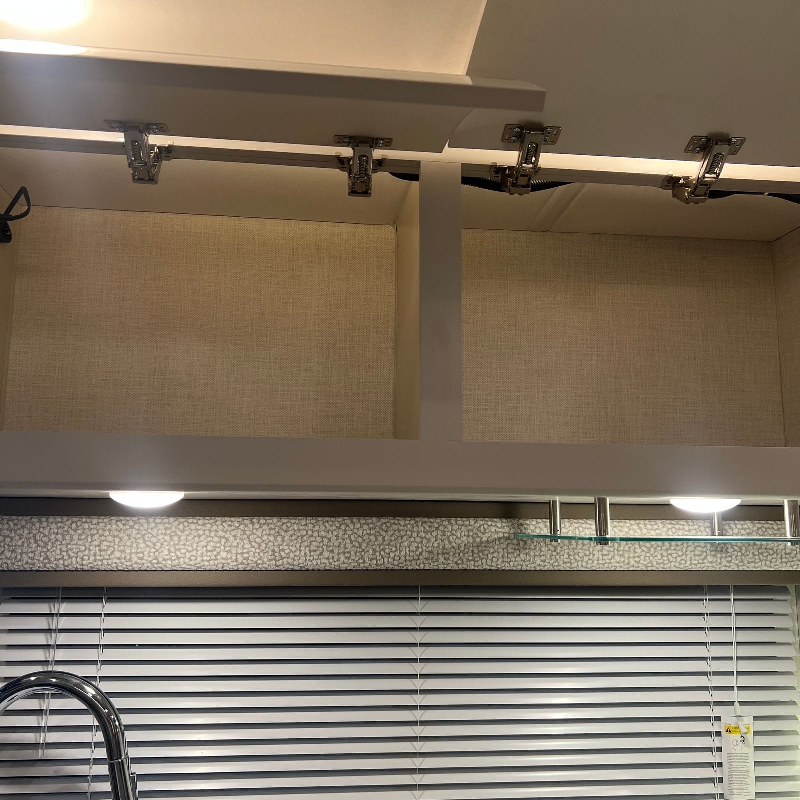 2026 Thor Delano 24XL open overhead galley cabinet showing the lined interior, soft-close hinges, under-cabinet lighting and a glass display shelf