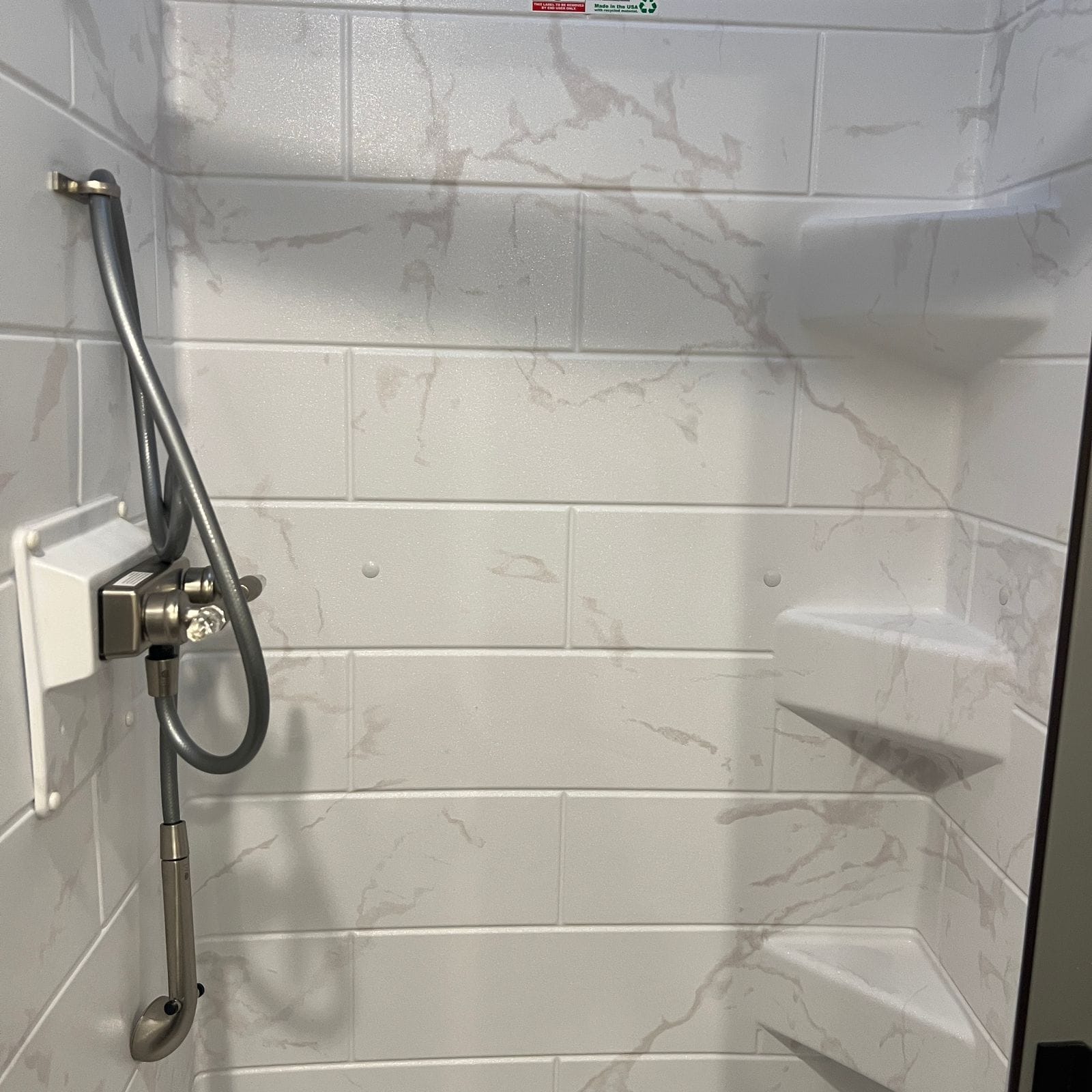 2026 Thor Delano 24XL shower interior showing marble-look tile-pattern walls, molded corner shelves and the brushed-nickel valve