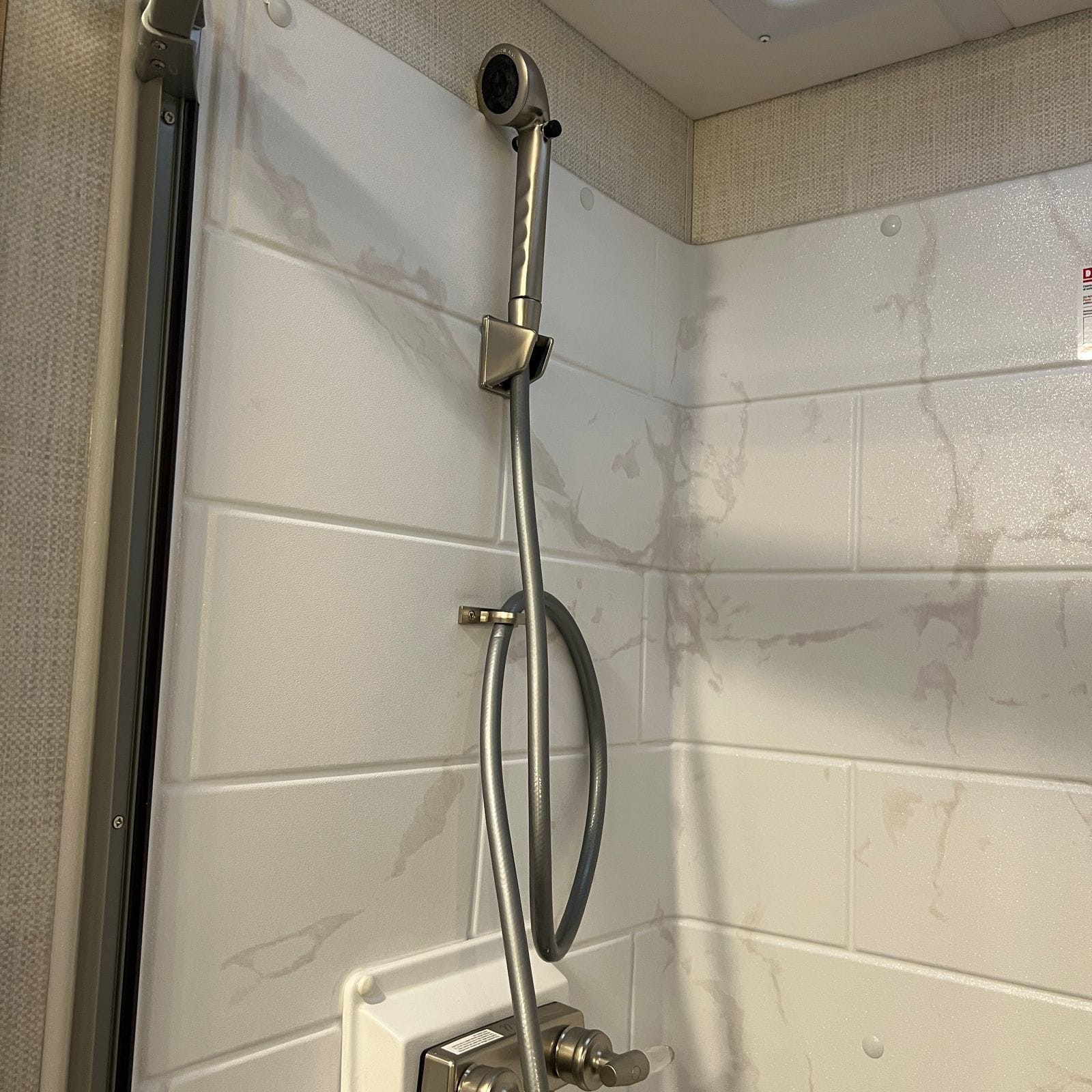 2026 Thor Delano 24XL shower with a brushed-nickel handheld showerhead on a slide bar and the framed glass shower door alongside