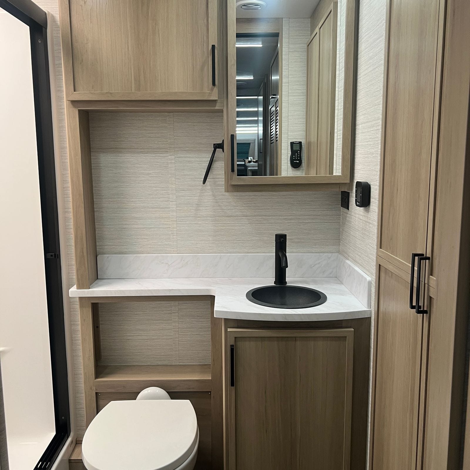 2027 Dynamax Europa S 37CA full bathroom view with toilet, corner vanity, mirrored medicine cabinet, open shelving, tall linen cabinet and the shower enclosure at left