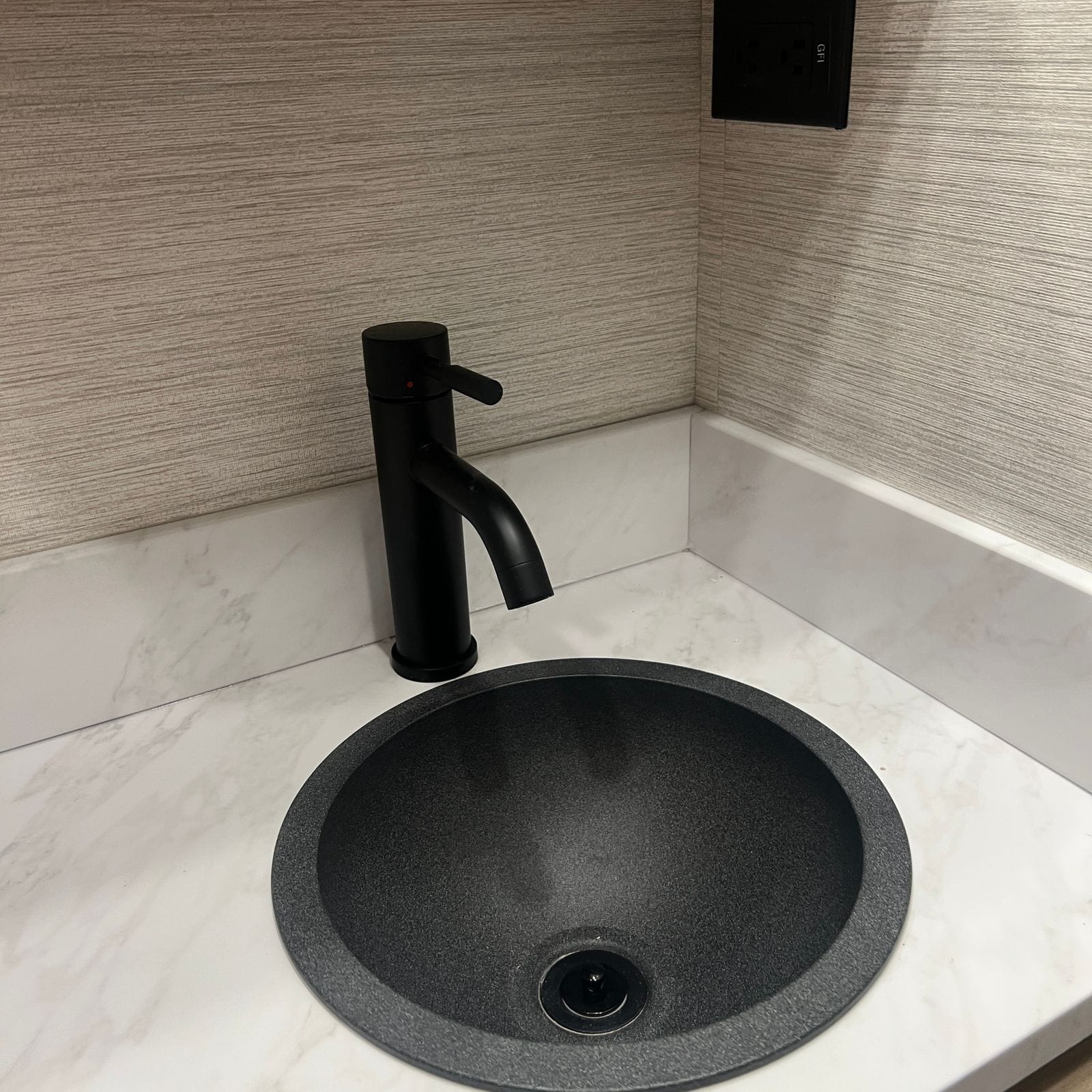 2027 Dynamax Europa S 37CA close-up of the bathroom's round grey granite-look basin with a matte black single-handle faucet on a marble-look counter