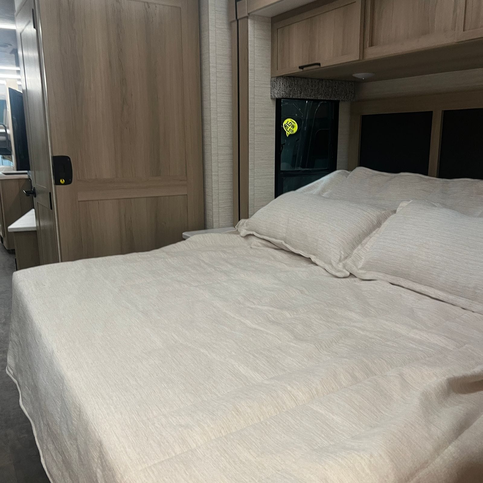 2027 Dynamax Europa S 37CA rear bedroom with a king bed made up in cream textured bedding, overhead cabinets, side window and a light wood door to the living area