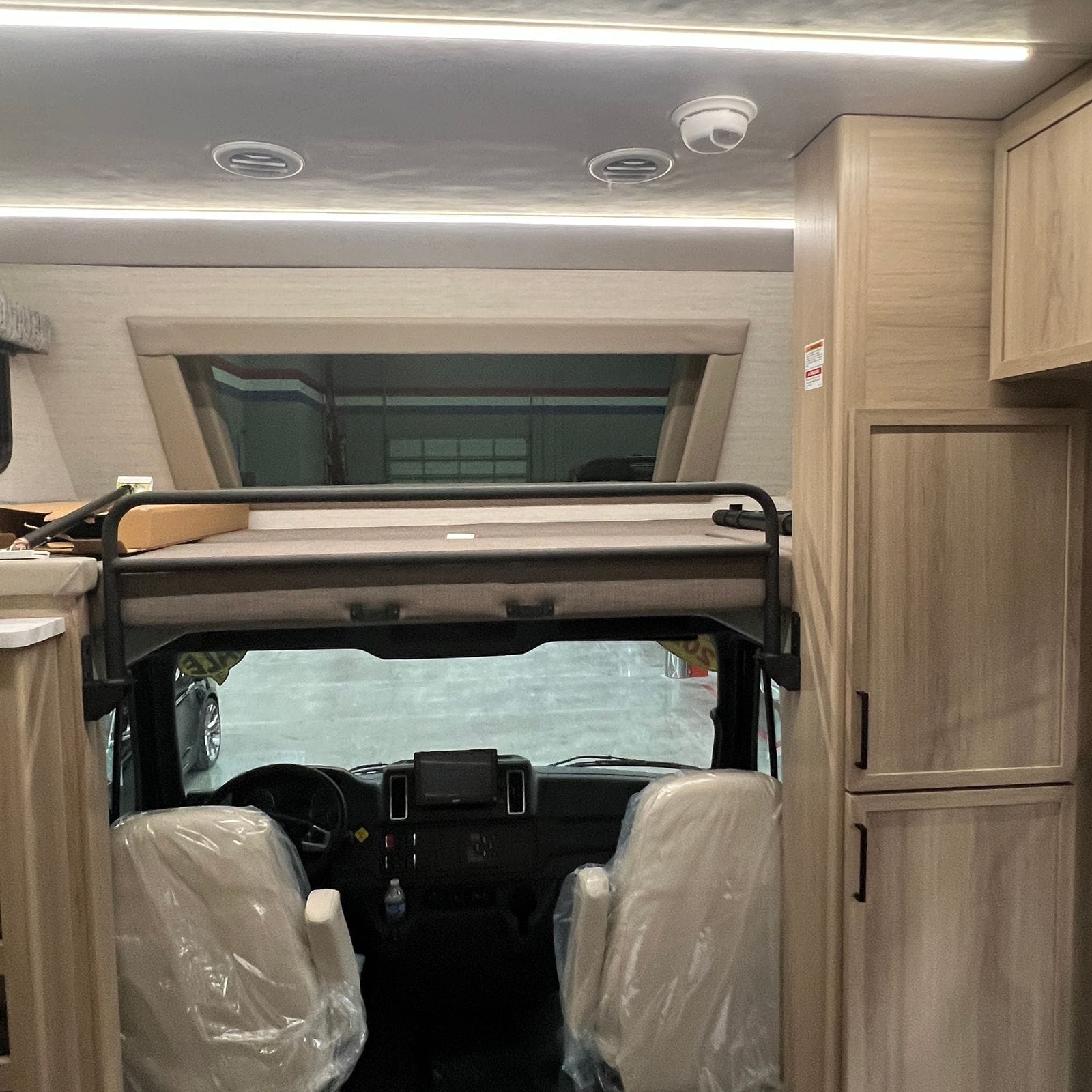2027 Dynamax Europa S 37CA closer forward view of the drop-down overhead cab-over bunk with black safety rail above the cab seats and dashboard