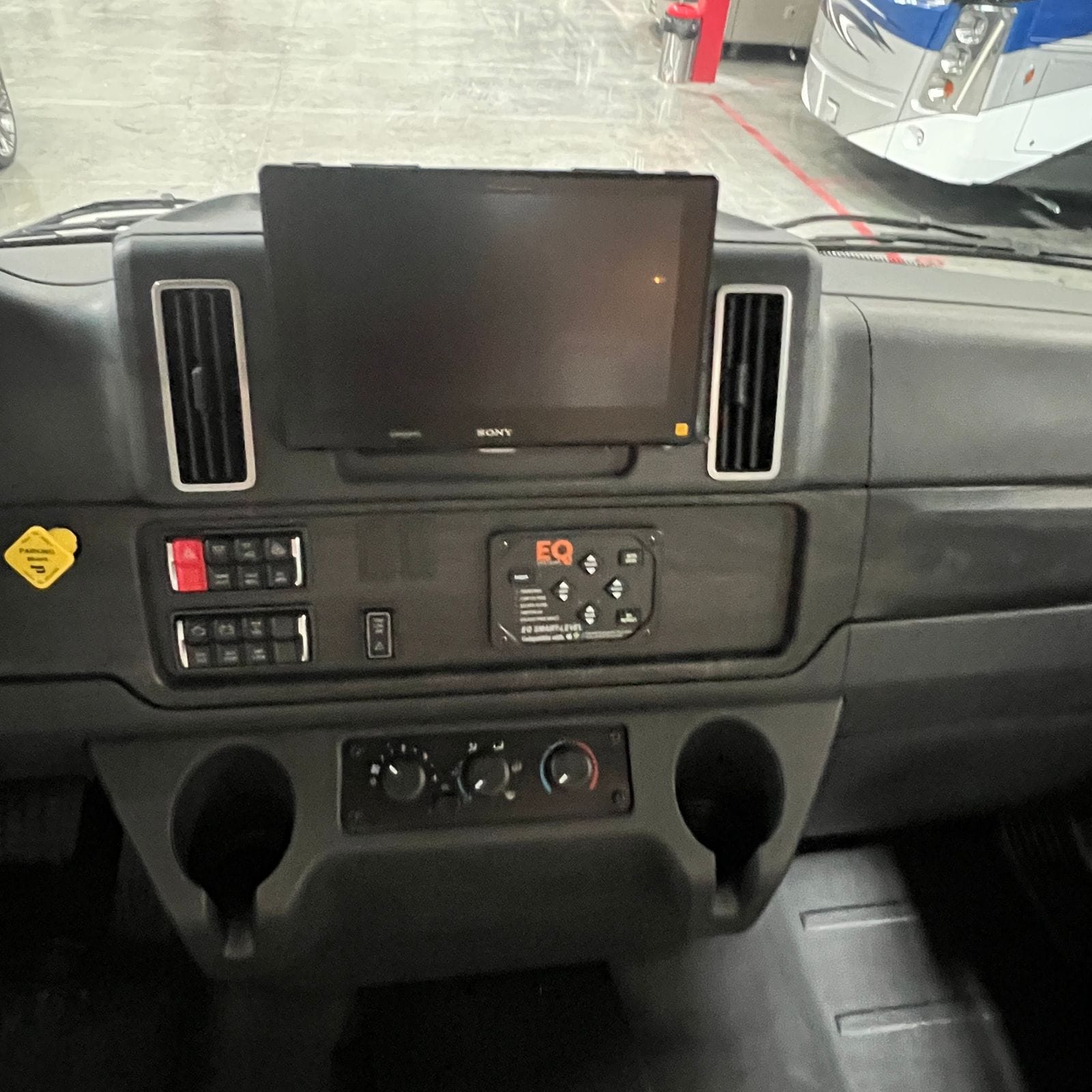 2027 Dynamax Europa S 37CA center dash with a touchscreen head unit, chrome-trimmed air vents, switch banks, a smart-level control pad, climate controls and two cup holders