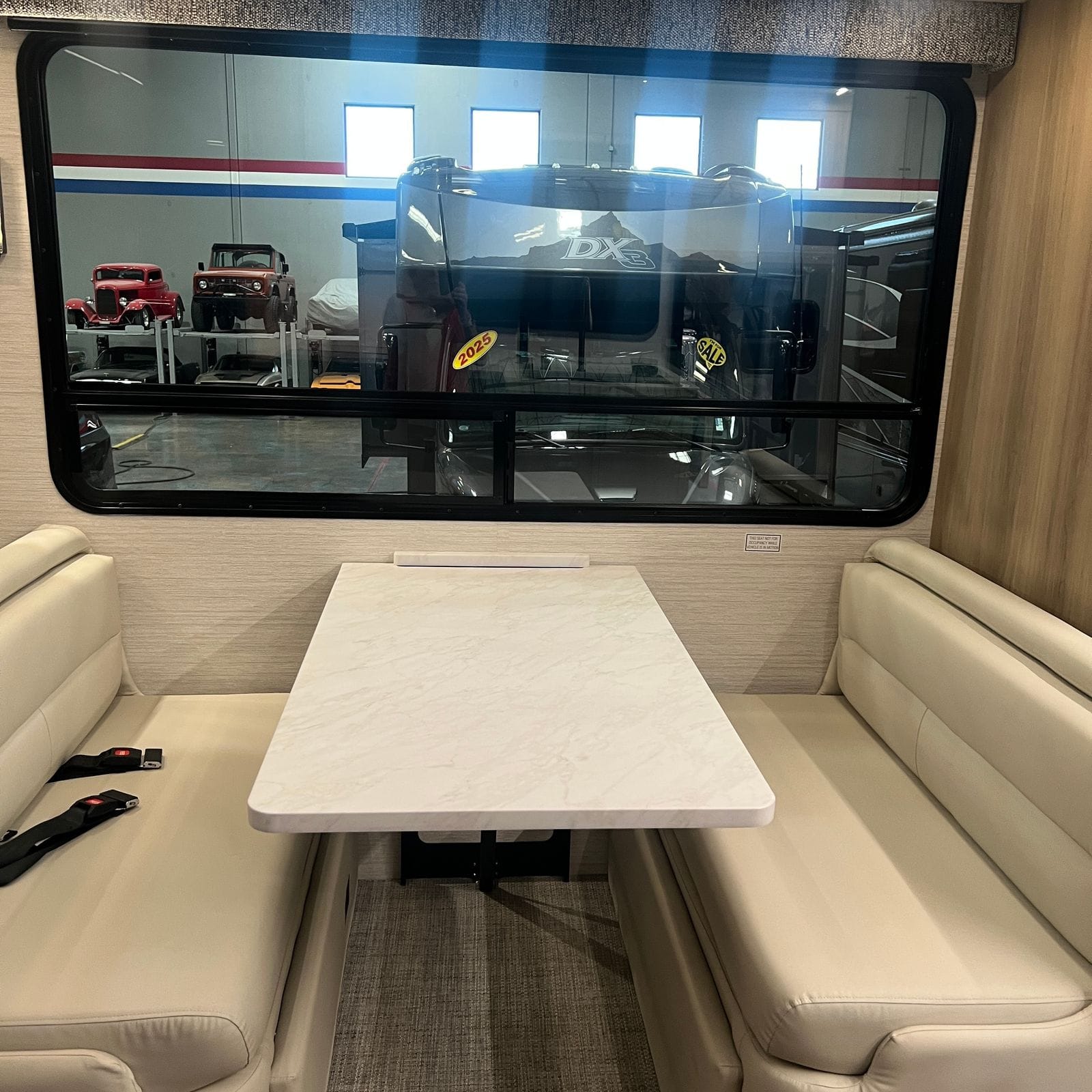 2027 Dynamax Europa S 37CA booth dinette with facing Alabaster leather bench seats, seat belts, a marble-look table and a large tinted window