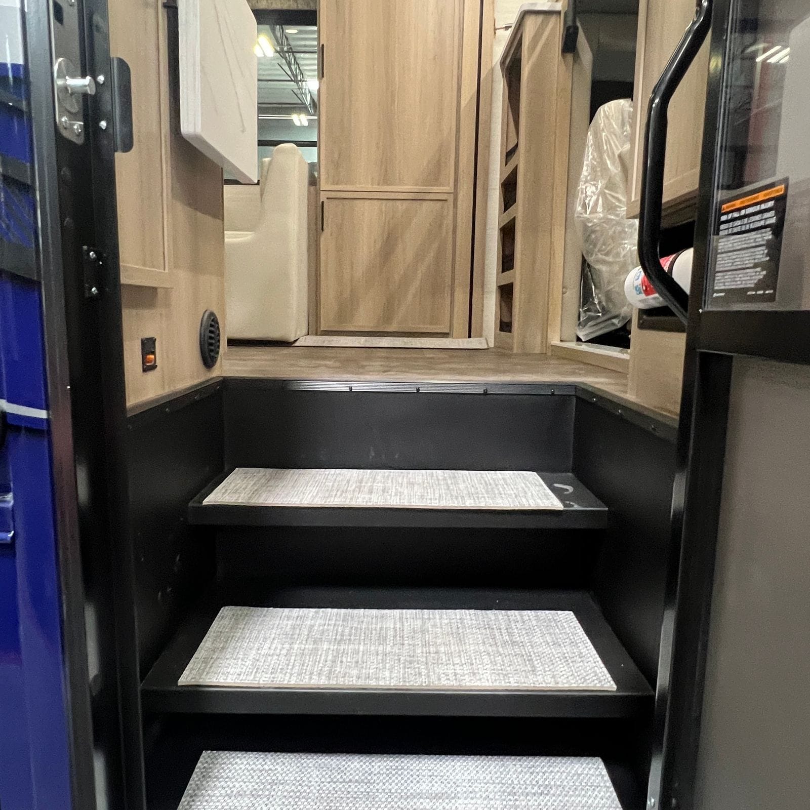 2027 Dynamax Europa S 37CA view up the entry doorway showing three carpeted steps, black step risers, light wood cabinetry and a grab handle at the top landing