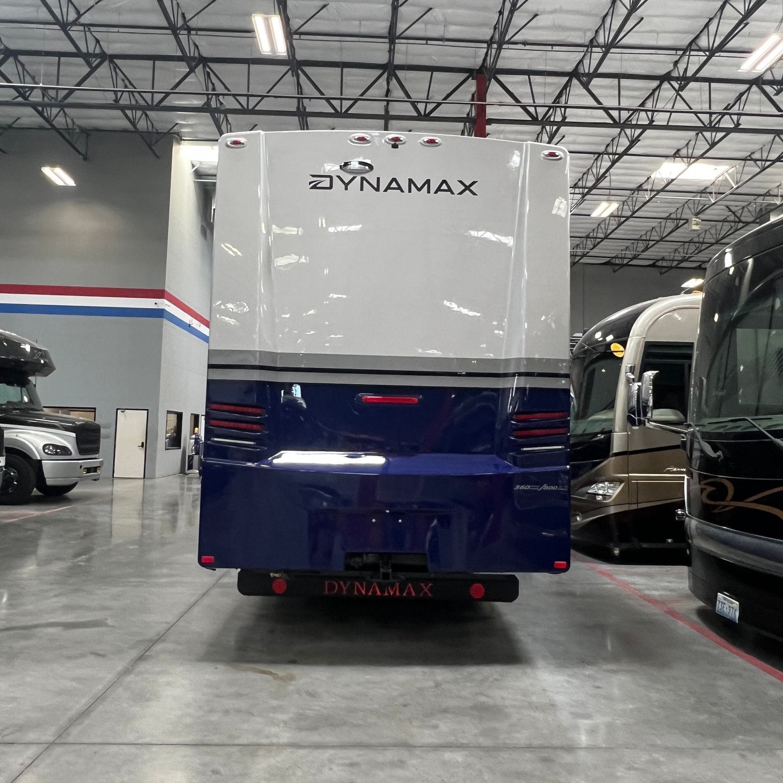 2027 Dynamax Europa S 37CA in Cobalt blue, straight-on rear view with white upper cap and Dynamax lettering, vertical LED tail light clusters and a black rear bumper with hitch receiver