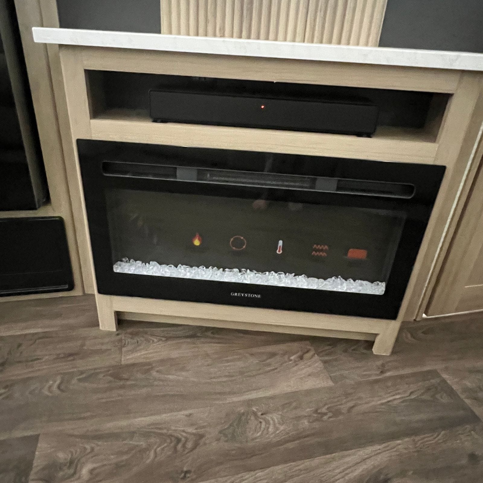2027 Dynamax Europa S 37CA electric fireplace insert with a crystal ember bed and a soundbar on the shelf above, set in a light wood console with a marble-look top