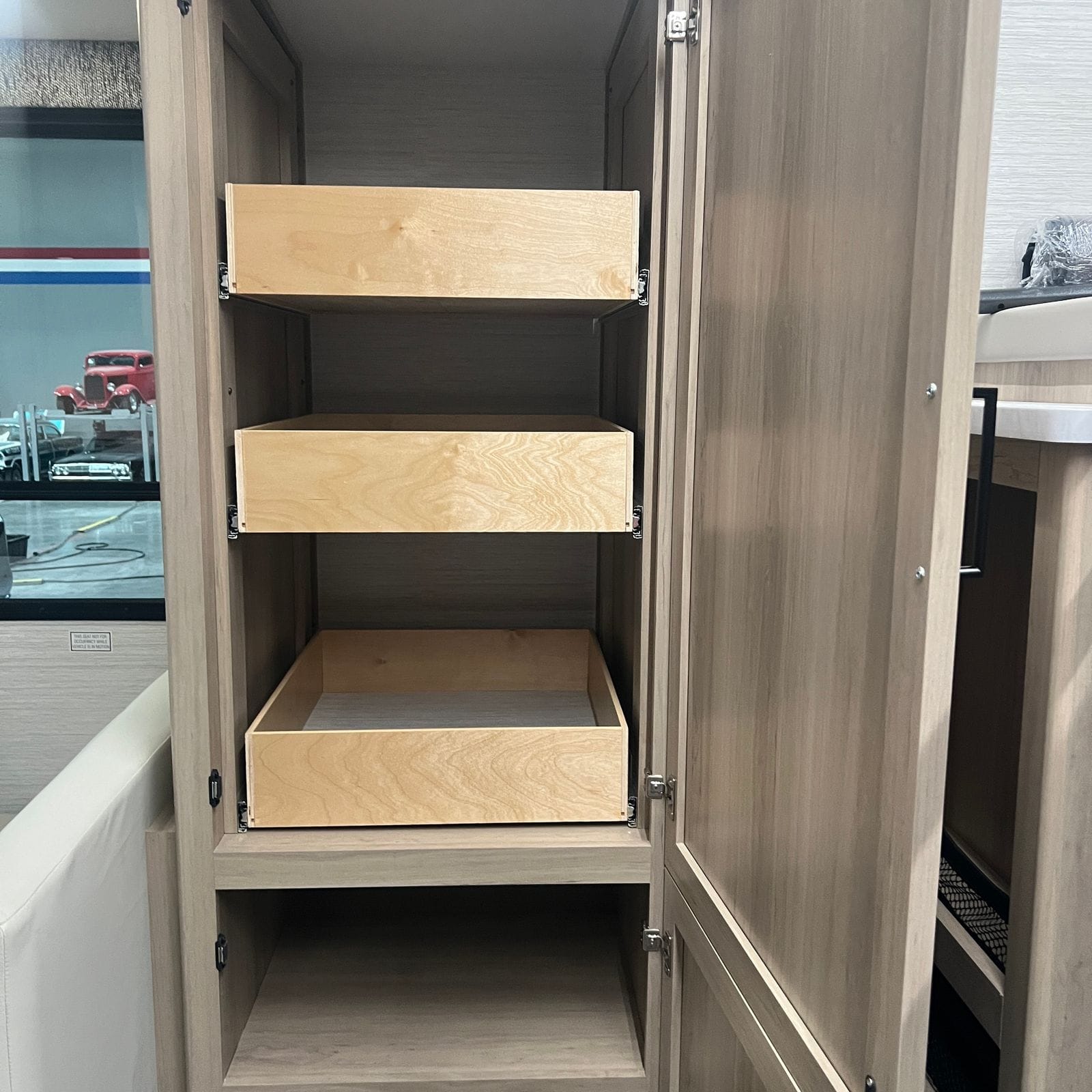 2027 Dynamax Europa S 37CA open tall pantry cabinet with three birch roll-out drawer trays and a lower shelf behind light wood doors