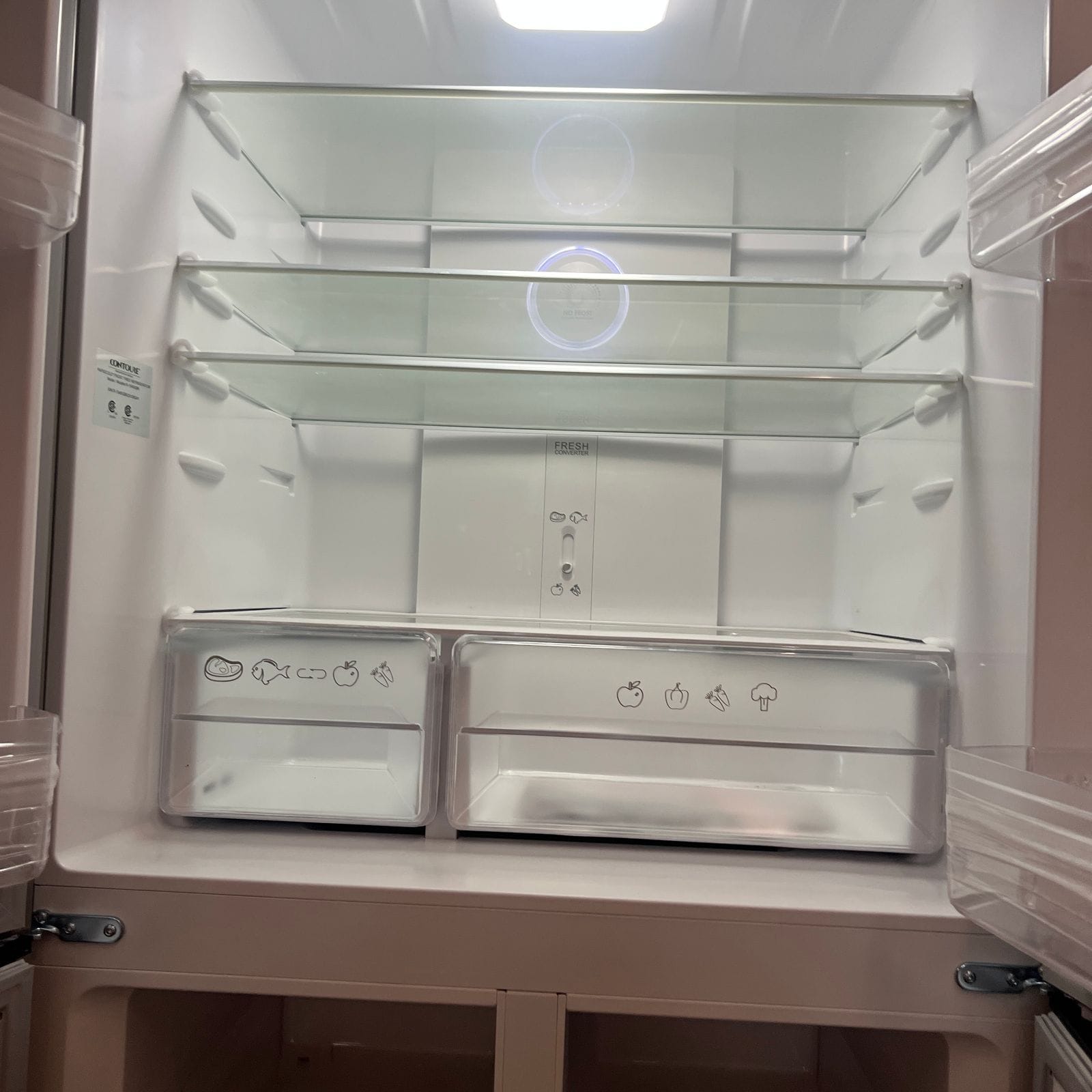 2027 Dynamax Europa S 37CA open refrigerator interior with three glass shelves, two clear crisper drawers and interior lighting