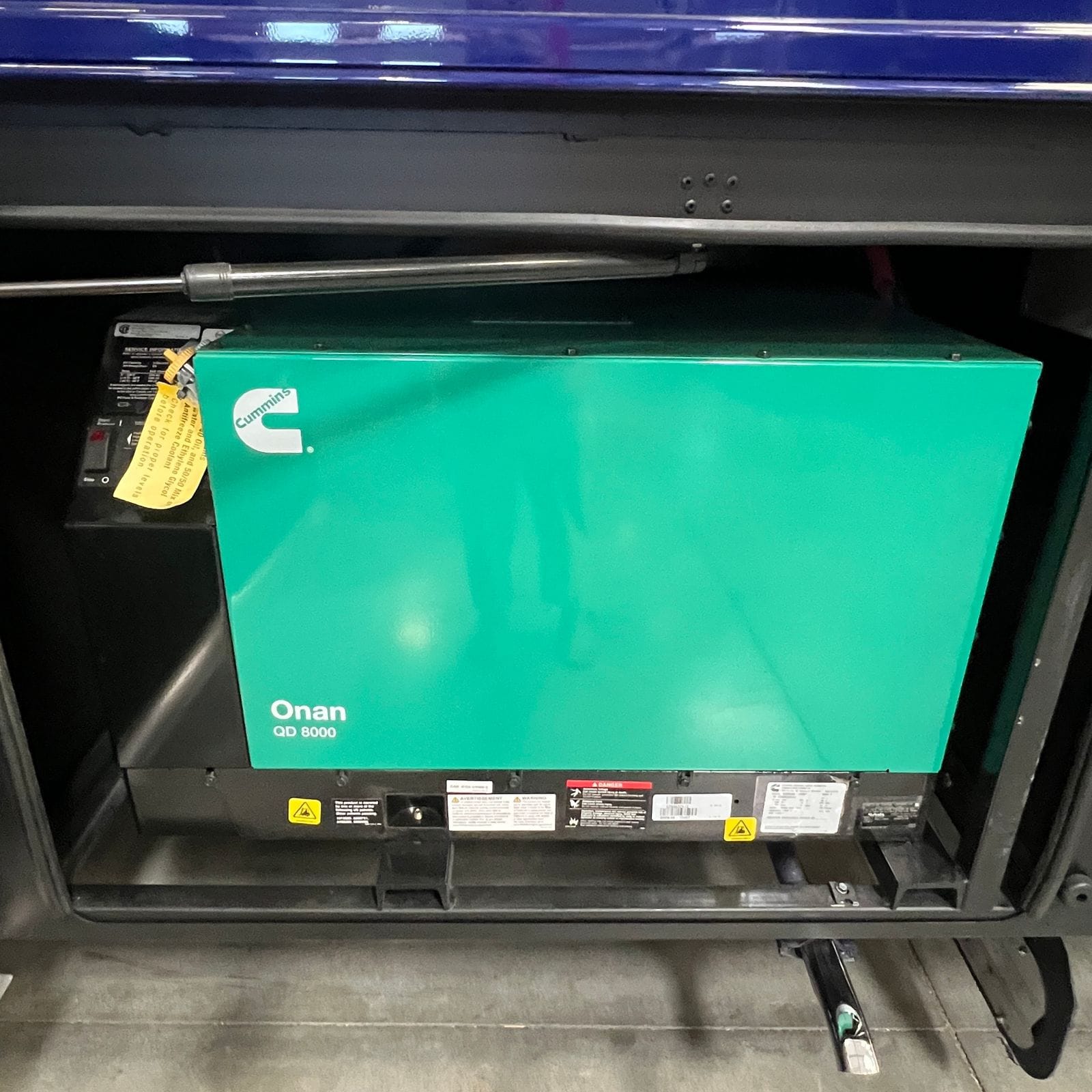 2027 Dynamax Europa S 37CA open lower bay showing a Cummins Onan QD 8000 diesel generator with its start and stop control panel