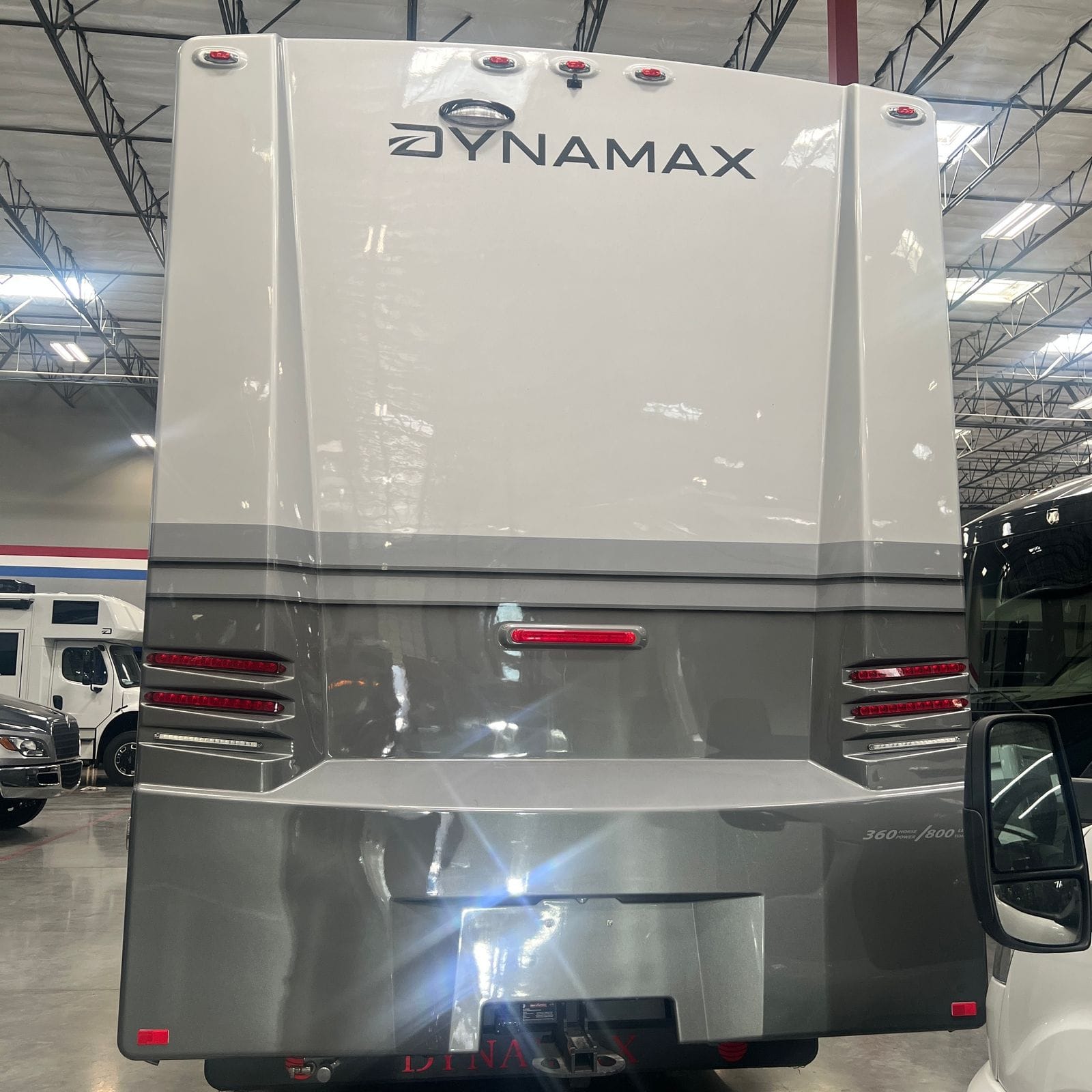 2027 Dynamax Europa S 37CA in Quicksilver, straight-on rear view showing the two-tone grey rear cap with Dynamax lettering, LED clearance and brake lights and a hitch receiver
